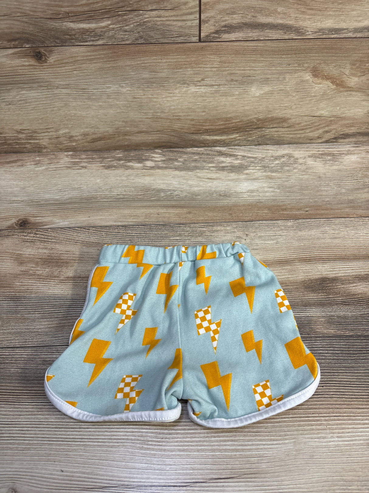 Flat-lay of Lucky Panda Kids blue lightning shorts with yellow and checkered lightning bolts, elastic waist and white trim on wood