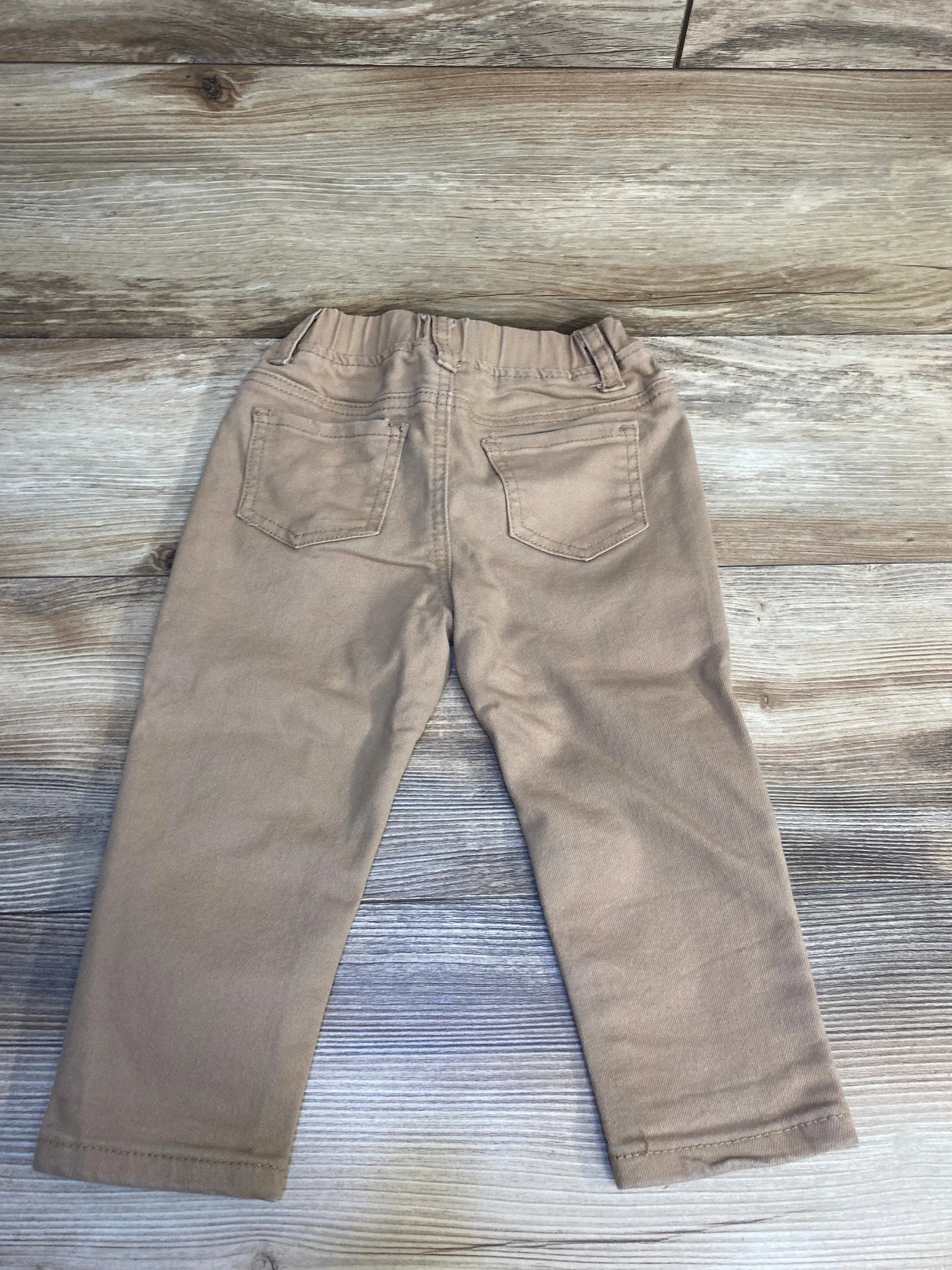 Light brown toddler pants with back pockets on a wood background, kids clothing resale