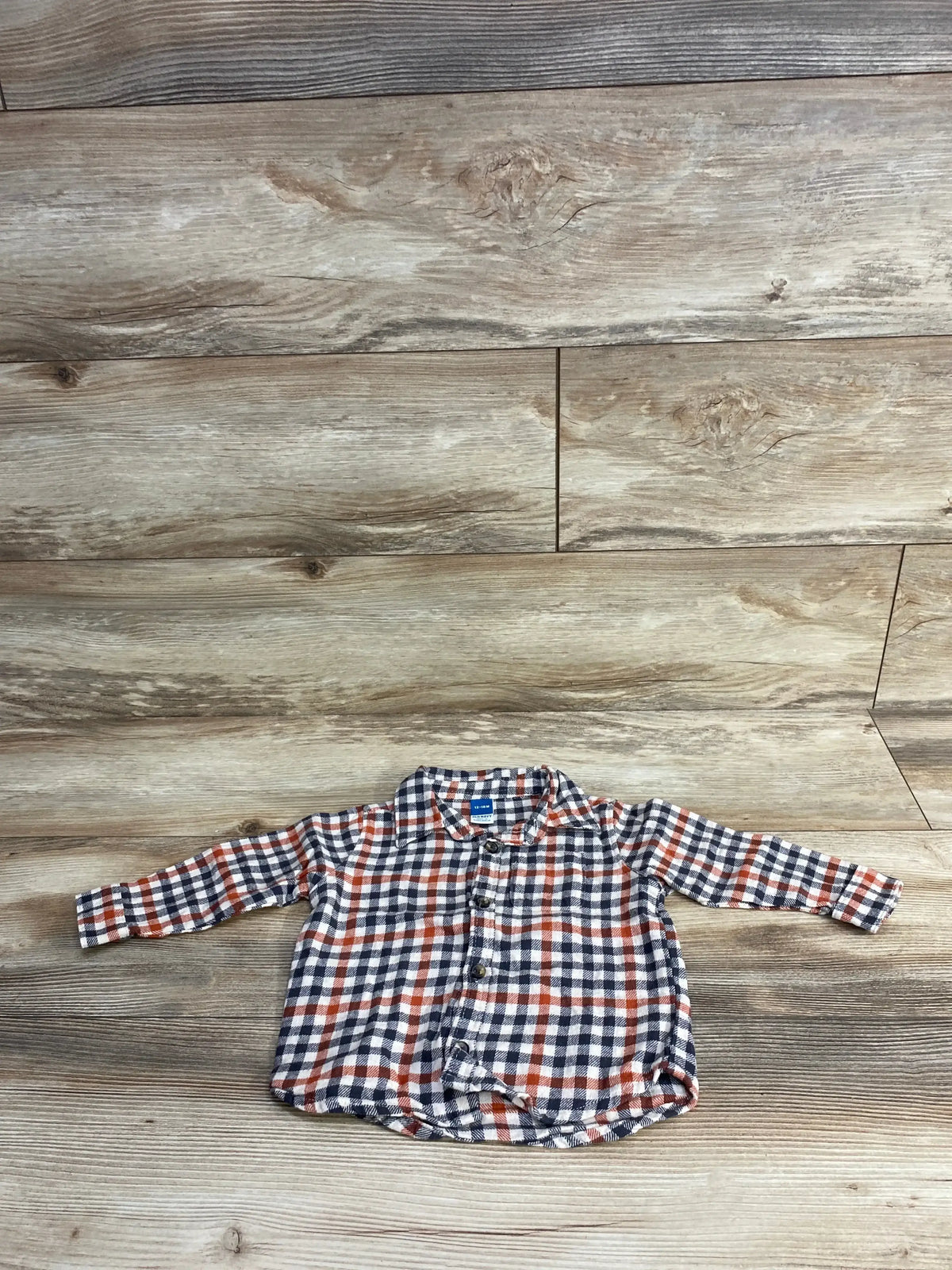 Plaid long-sleeve baby shirt with button front in blue, red, and white on wood floor.