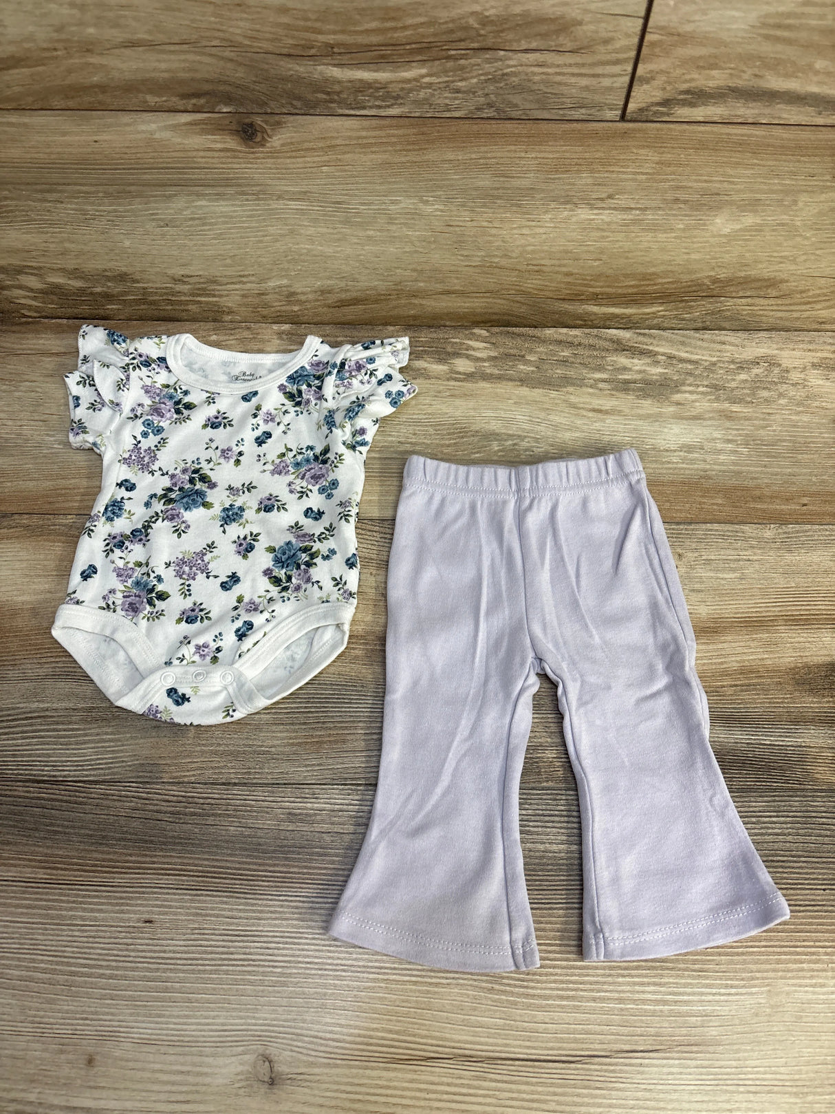 Baby girl's floral printed onesie with ruffled sleeves and light purple flared pants on wooden floor