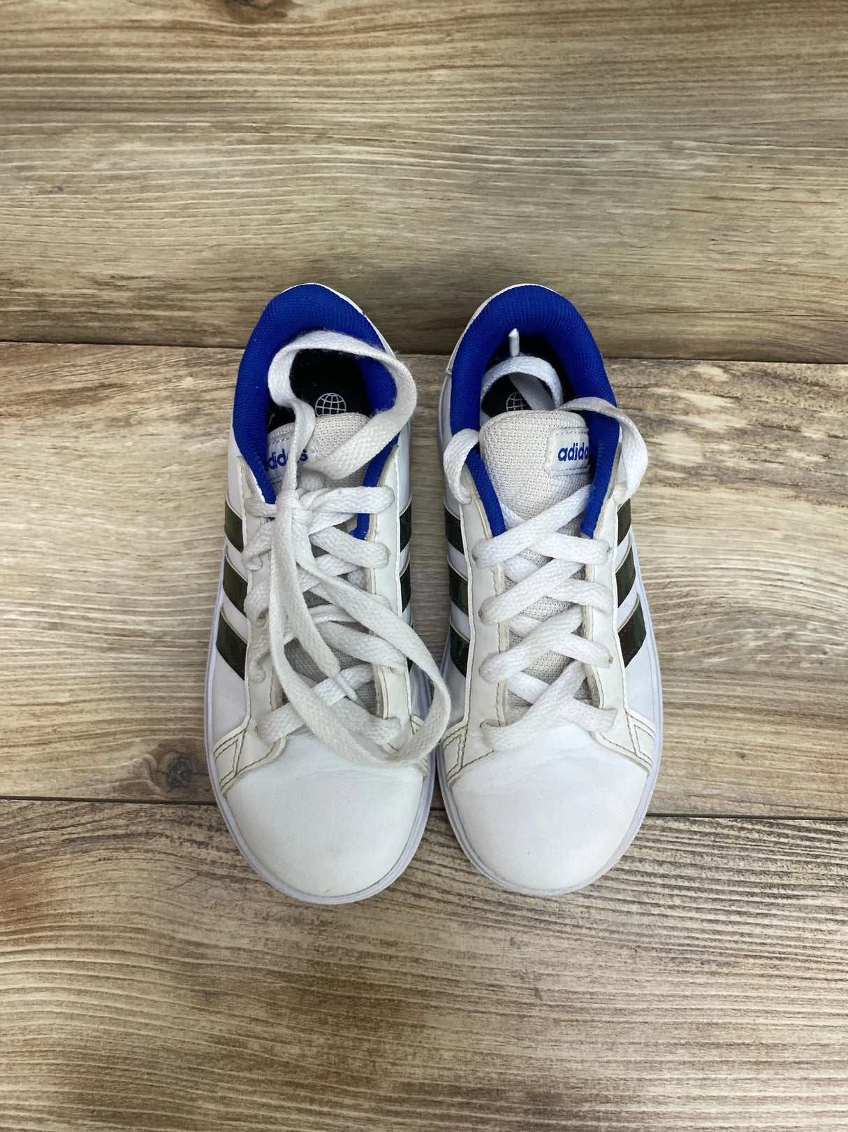 Top view of Adidas Neo Grand Court Base 2.0 toddler sneakers, white with royal blue collar, three black stripes, on light wood floor