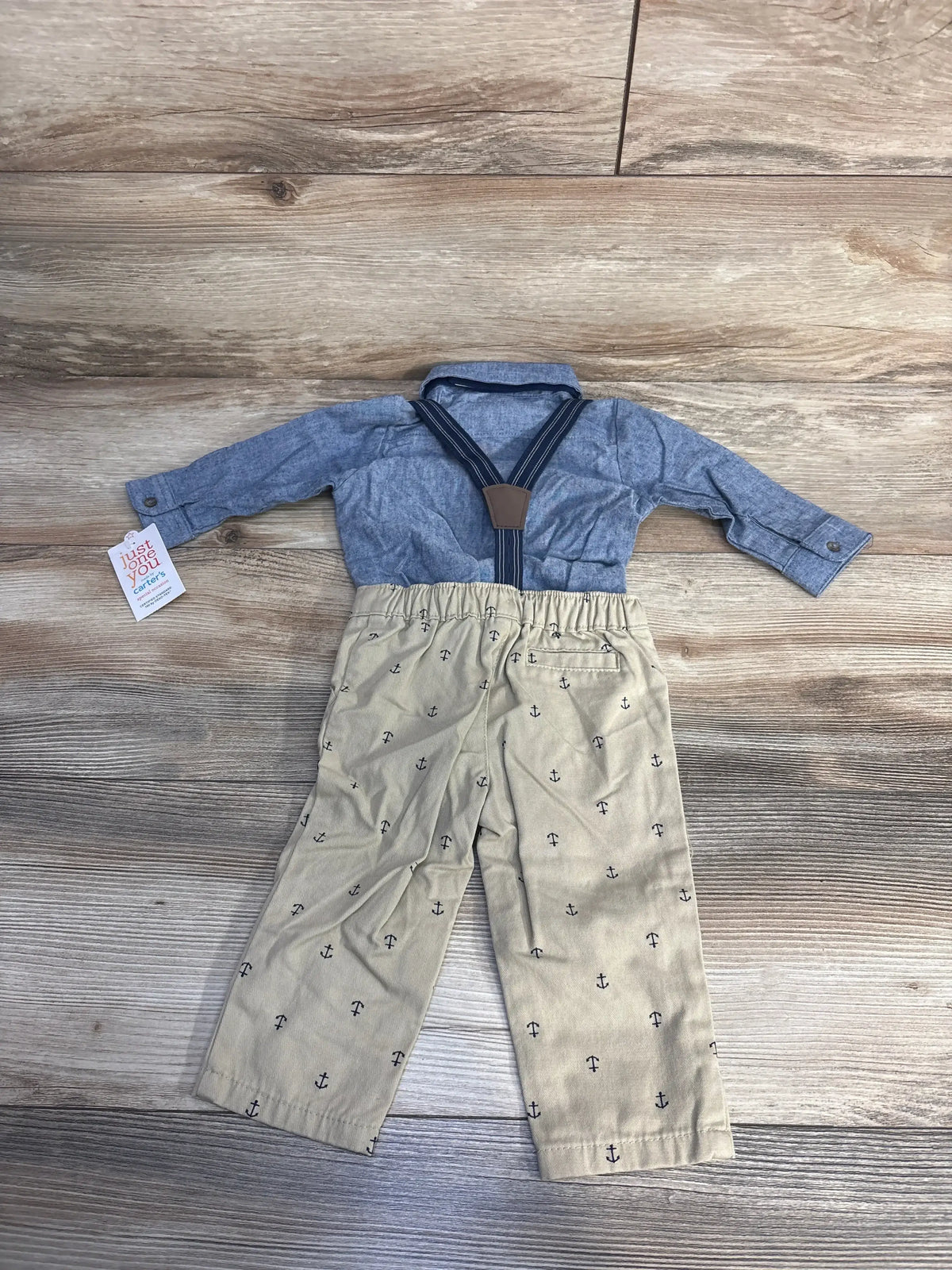 Toddler outfit with blue button-up shirt and beige anchor print pants with suspenders on wood floor