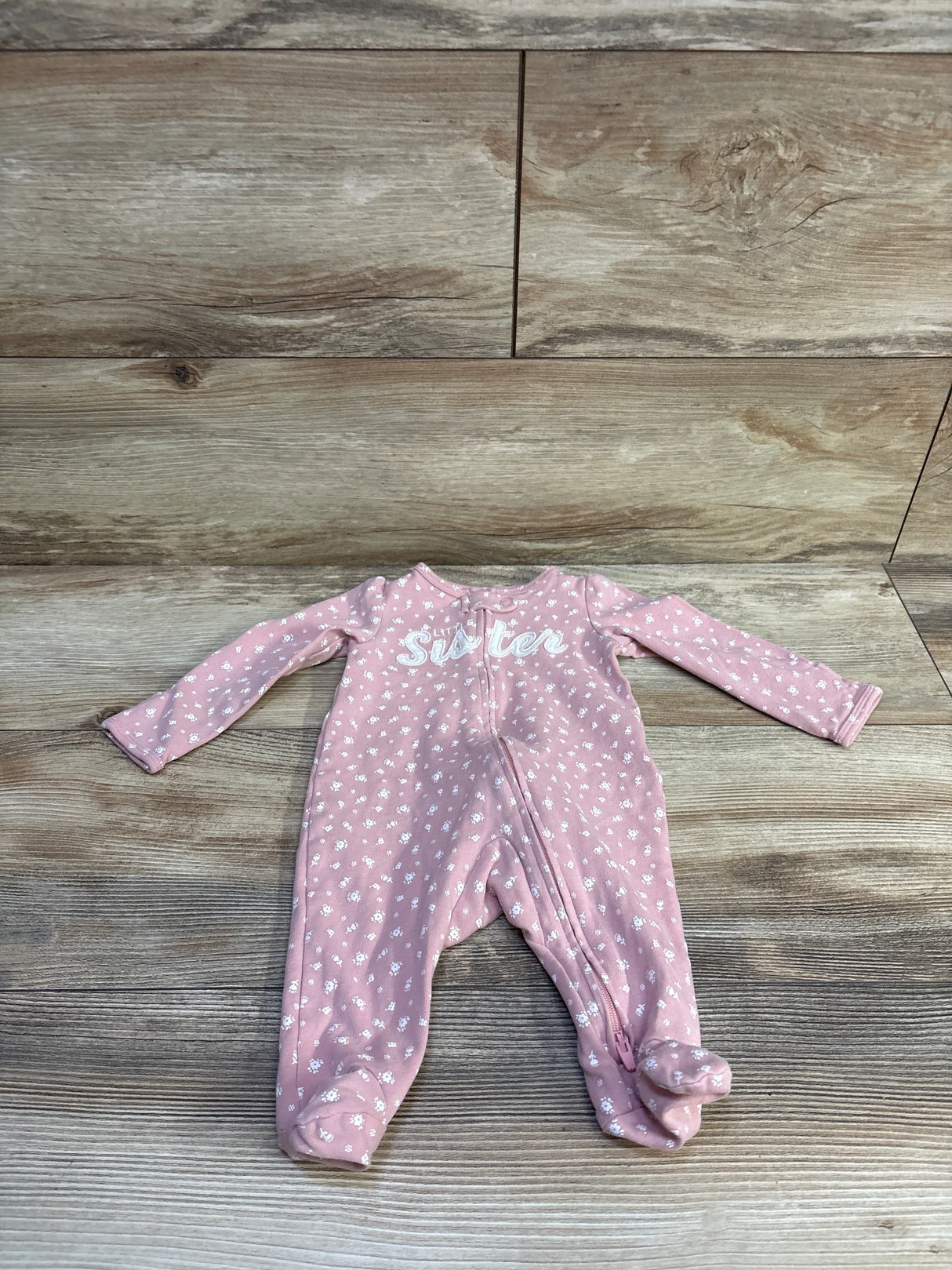 Front view of pink footed sleeper 3M with ‘Sister’ chest embroidery, white floral print and front zipper on wood background
