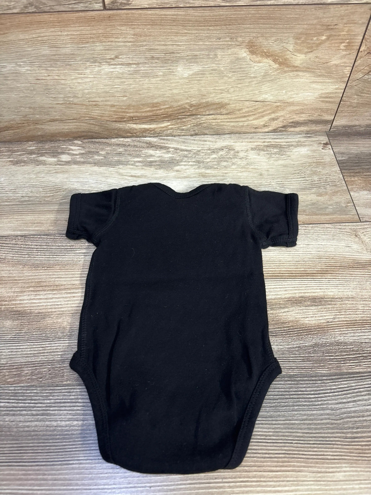Flat lay of Rabbit Skins New World Order black bodysuit in size 6 months, showing short sleeves on wood-look flooring