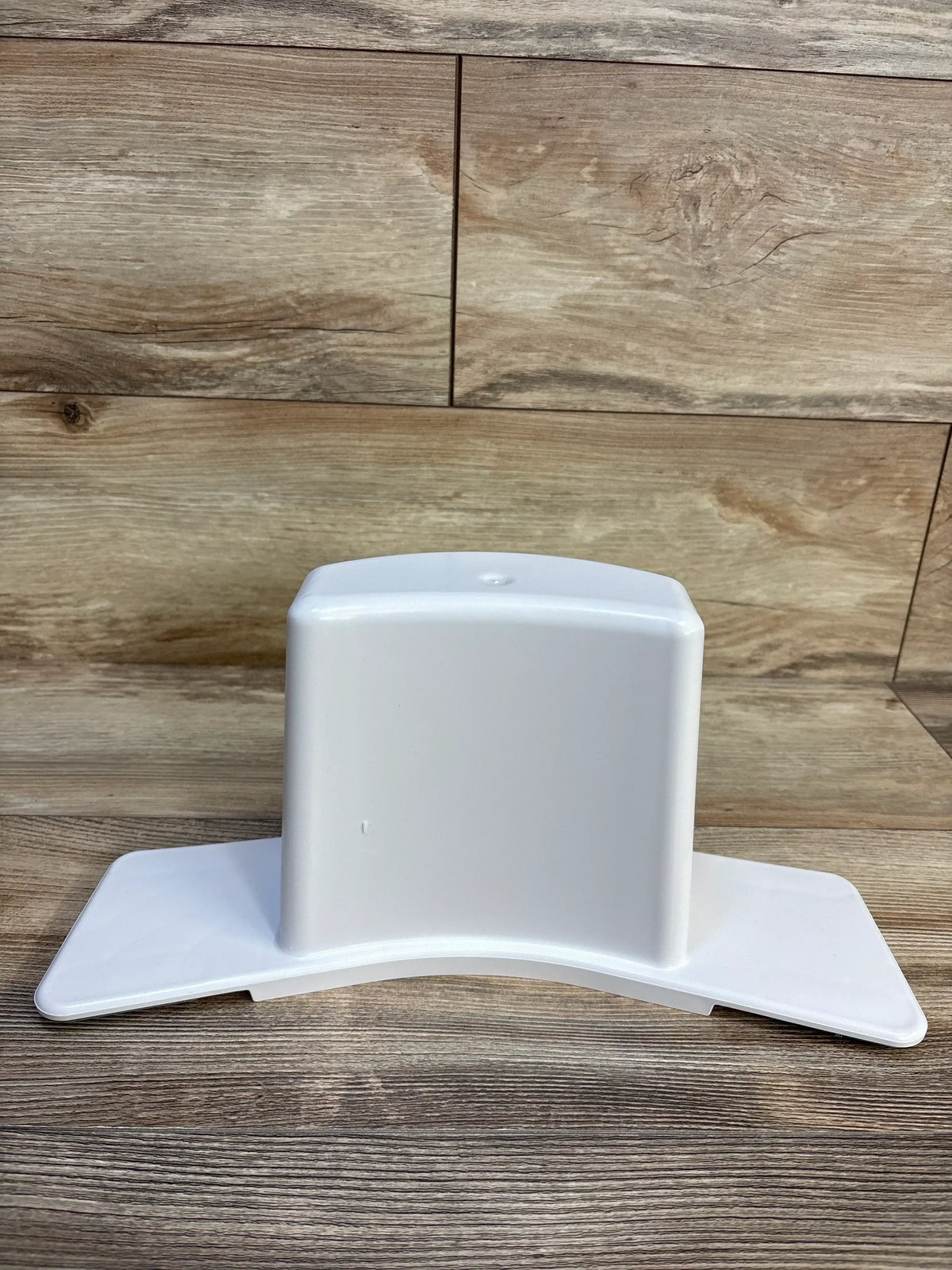 Front view of Super Potty Trainer adjustable back support showing white plastic curved base with side wings on wood floor background