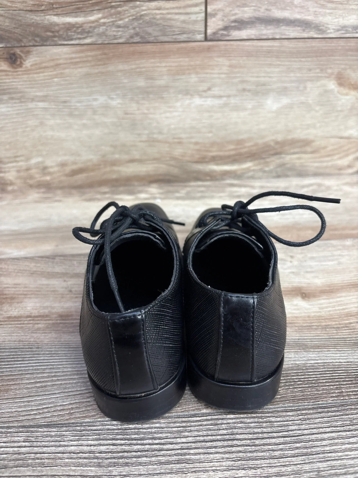 Back view of black leather dress shoes with textured pattern and laces on wooden floor