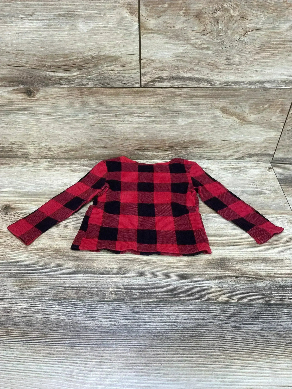 Flat lay of red and black buffalo check toddler thermal shirt showing long sleeves on light wood background