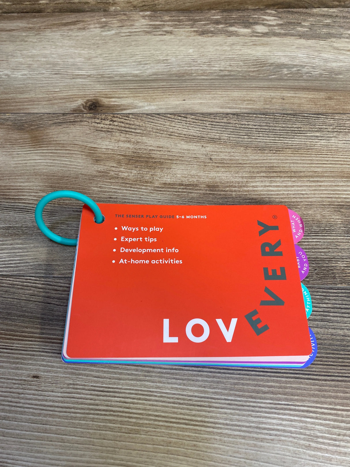 Lovevery sensory play guide for 5-6 months on wooden surface with a teal ring