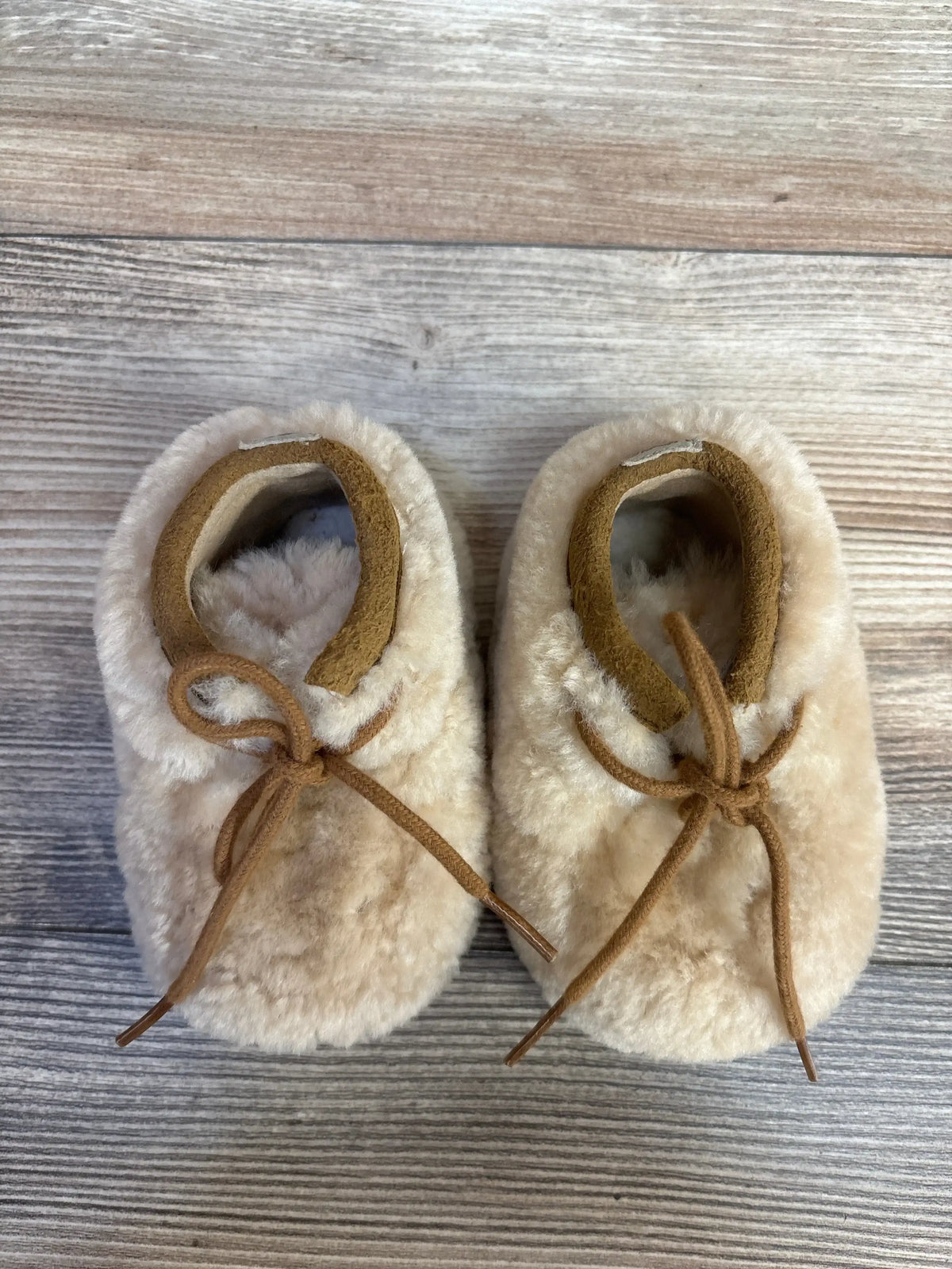 Fuzzy beige baby moccasins with leather laces on a wooden floor