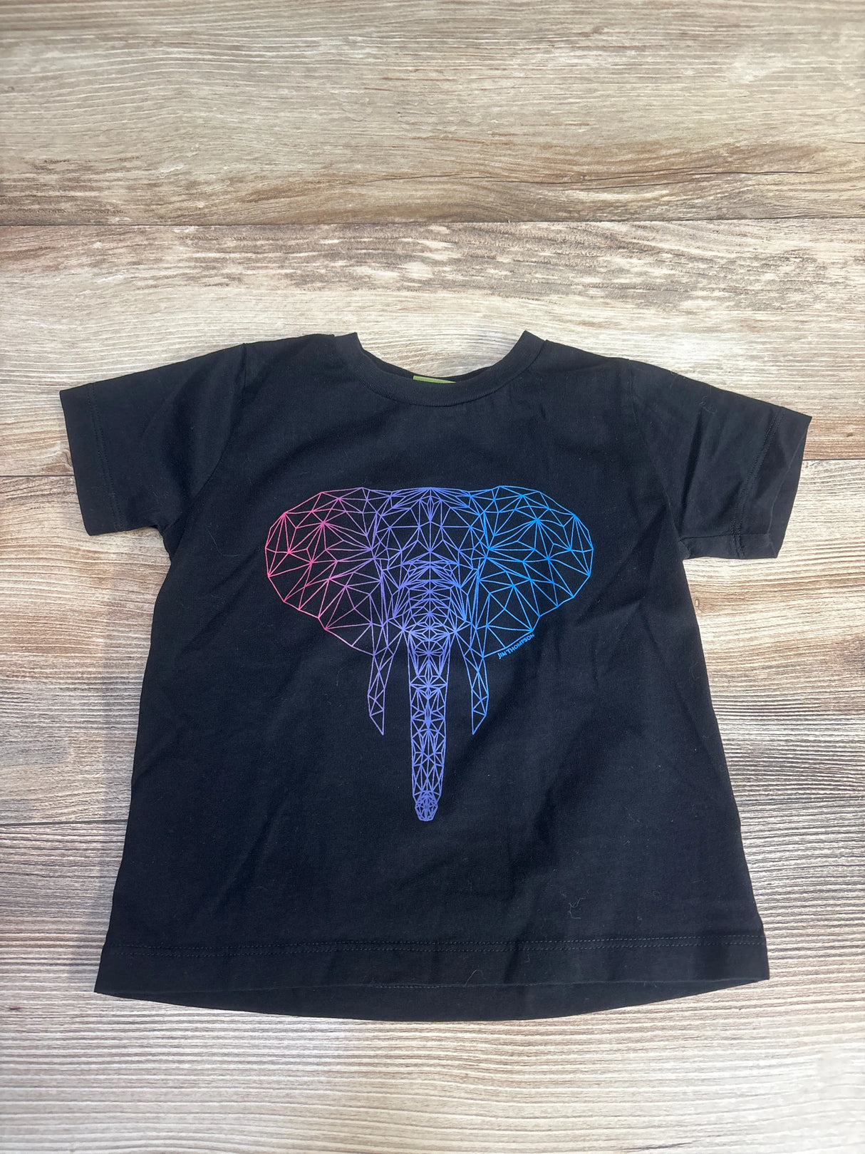Black t-shirt with colorful geometric elephant graphic on wooden background