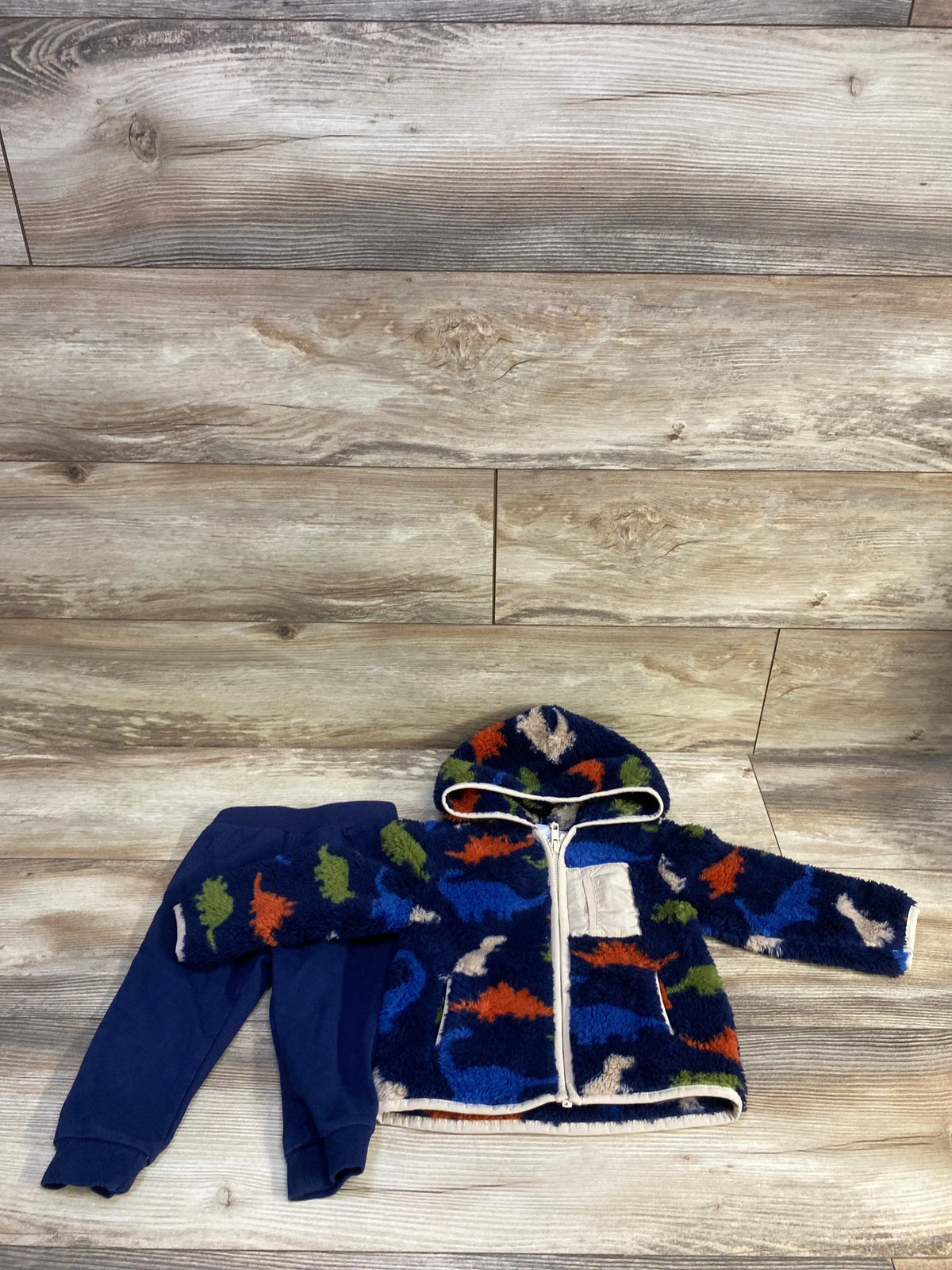 Flat lay of Little Me navy 2-piece (18m): faux-fur full-zip hooded jacket with multicolor dinosaur print and matching navy pants