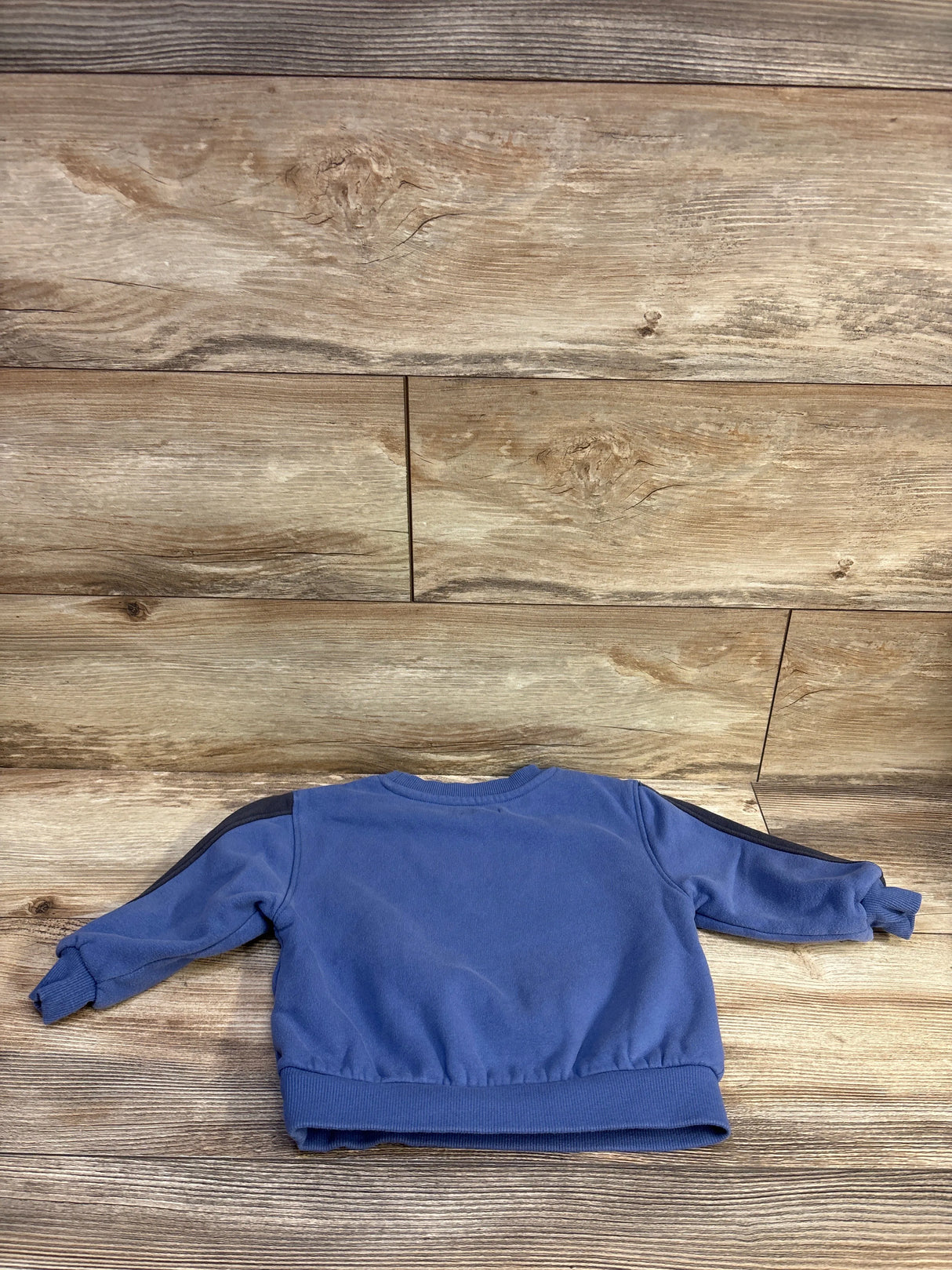 Back view of Grayson Mini blue pullover sweatshirt 2T showing ribbed cuffs, hem and black sleeve stripes on wood background