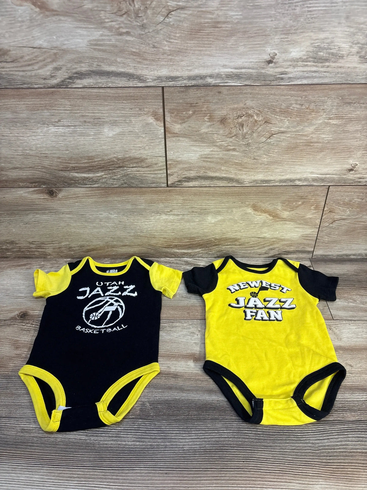 Utah Jazz themed infant bodysuits in black and yellow on wood background