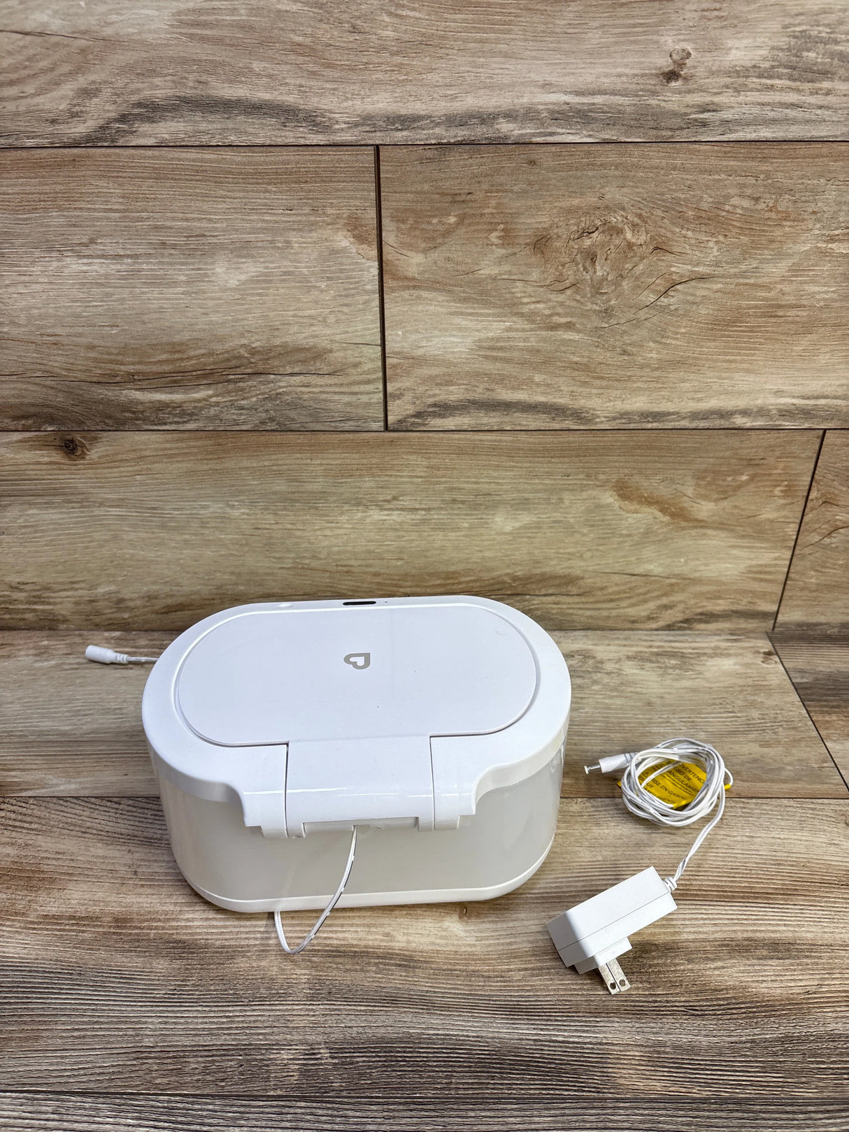 Angled front view of white Munchkin Touch Free Wipe Warmer showing sensor lid, nightlight, and power adapter on wood surface