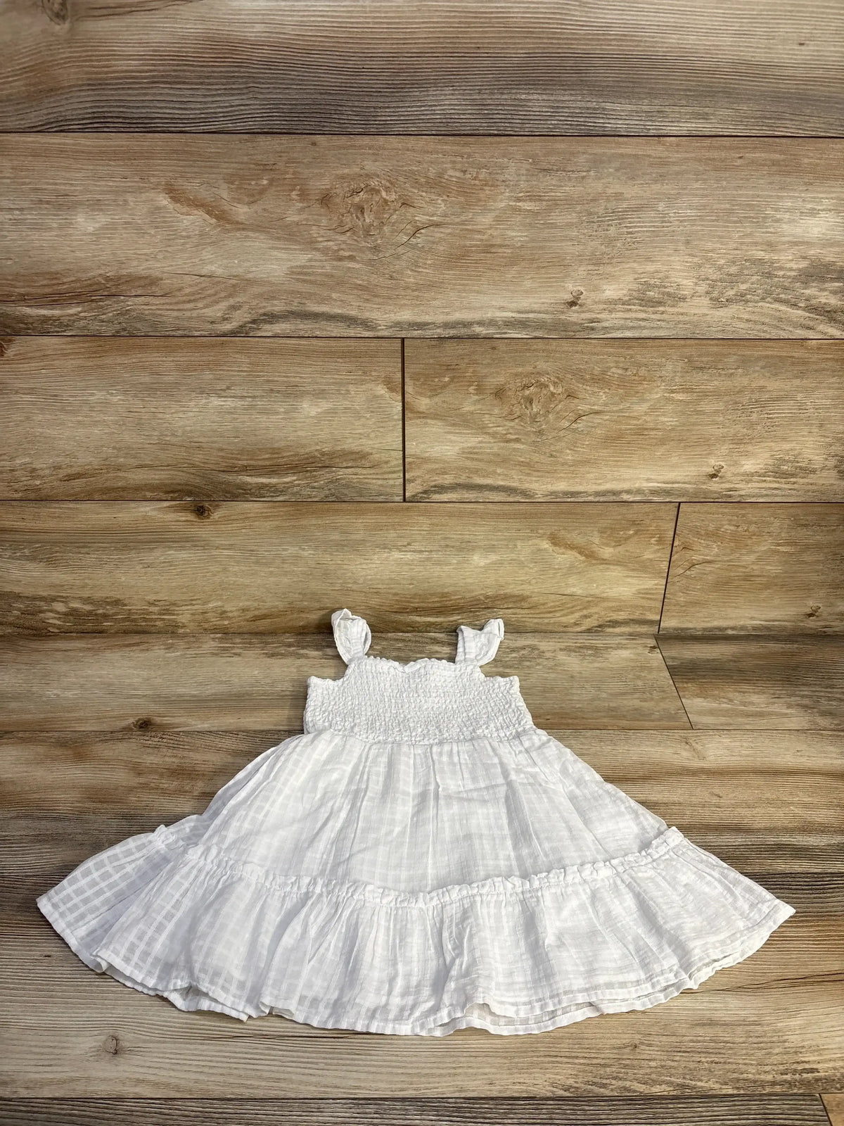 Front view of Janie and Jack Emily seersucker sundress in white showcasing smocked bodice tie straps and tiered ruffled skirt on wood plank floor