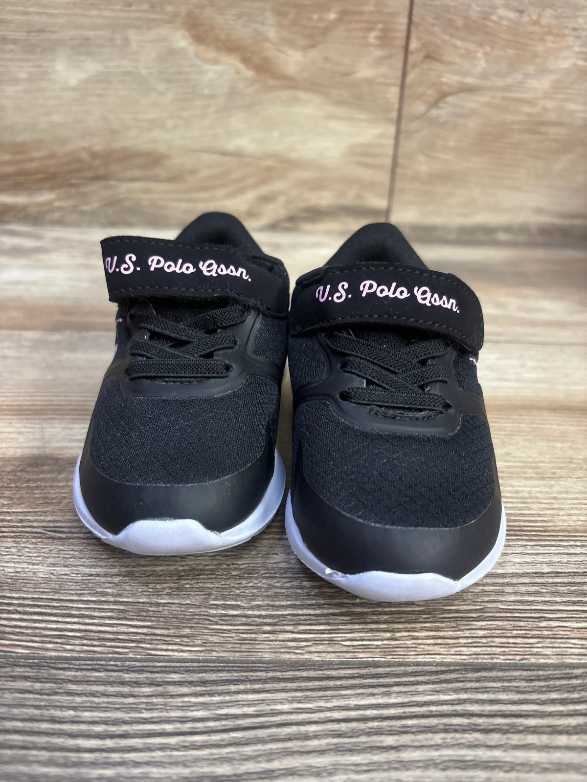 Front view of U.S. Polo Assn. black glitter sneakers showcasing black laces and white soles on a wood-grain surface