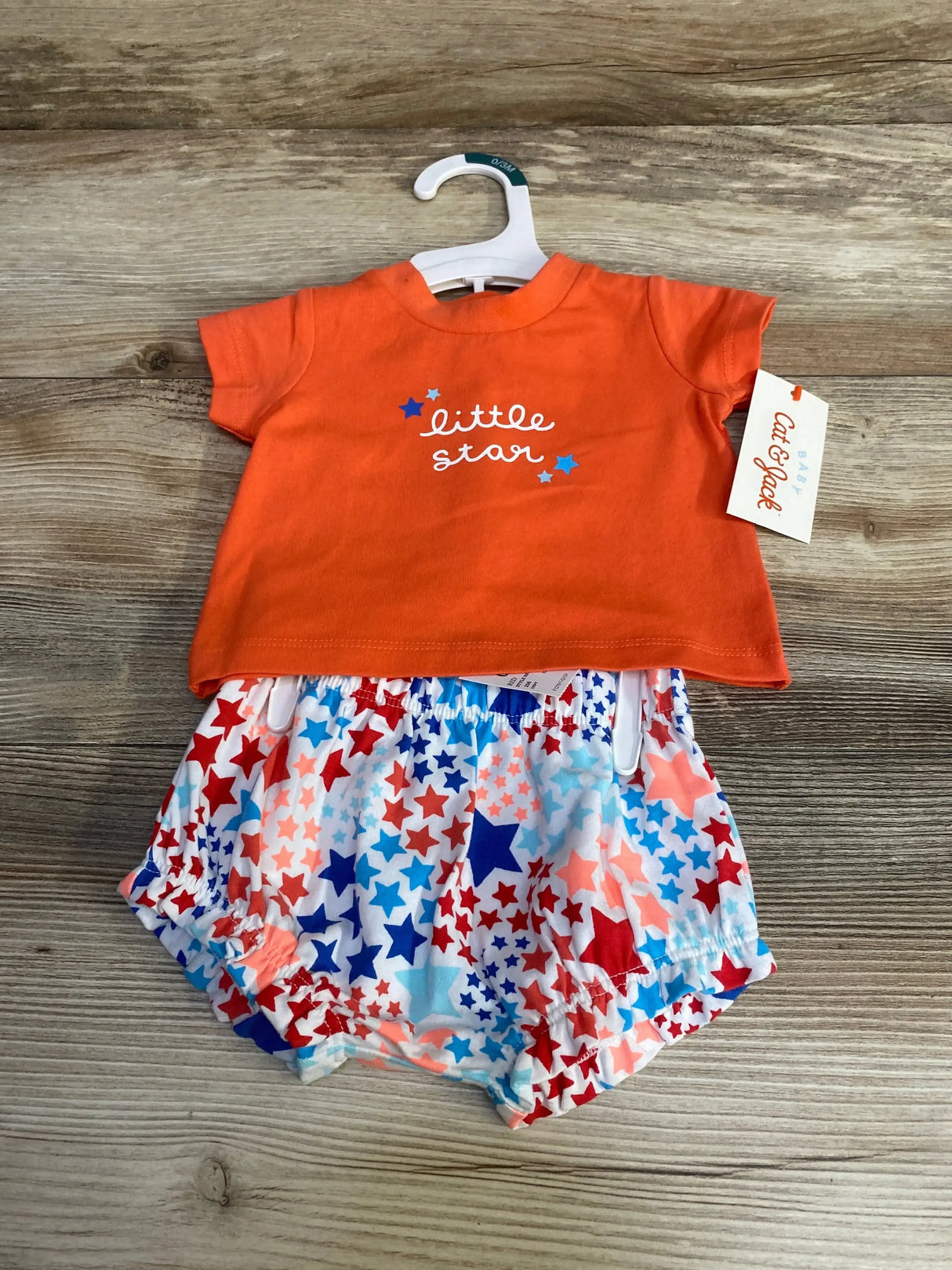 Top down view of newborn orange Little Star shirt and star print shorts showing star graphic and elastic waist on wood
