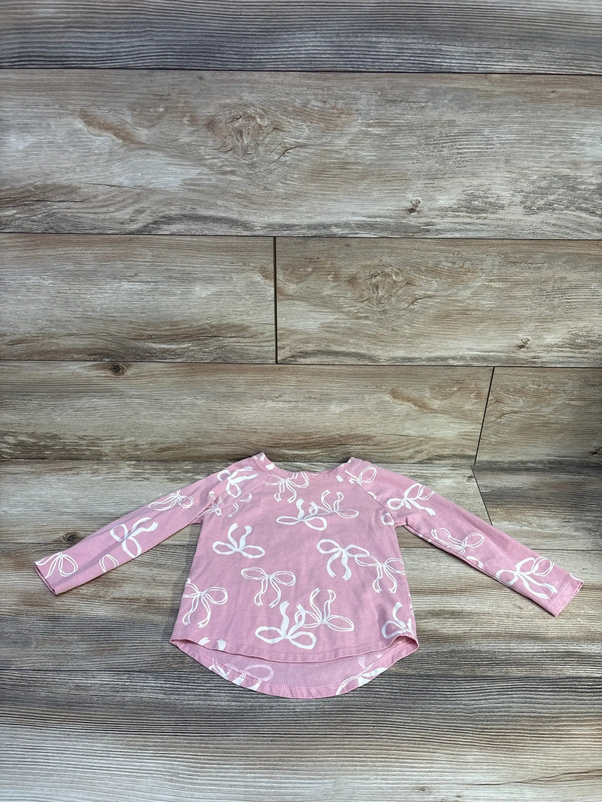 Front view of Cat & Jack pink long sleeve shirt in size 3T showcasing white bow print on a wood plank background