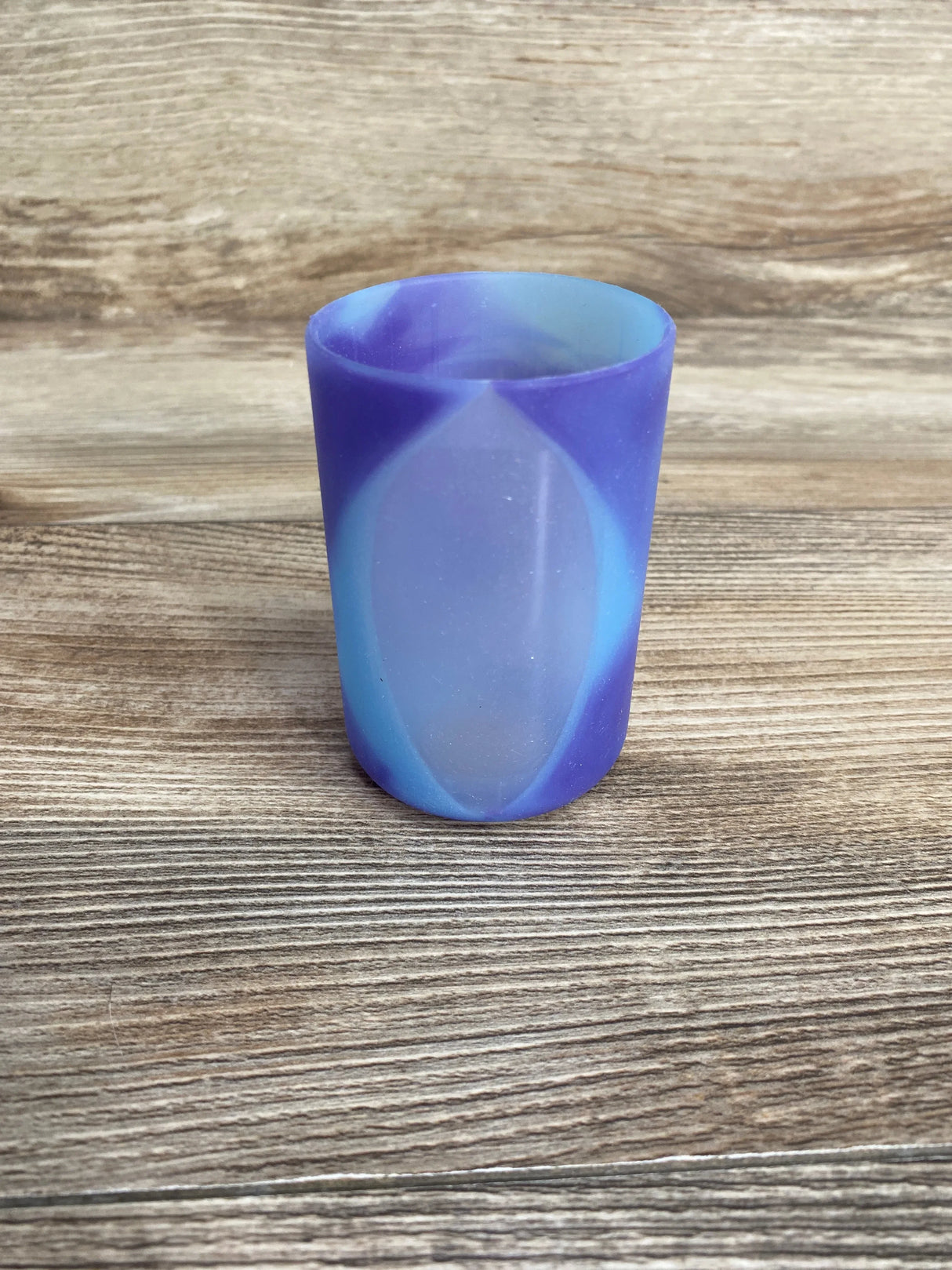 Front view of Dr. Brown's 4 oz bottle sleeve, purple-blue glow-in-the-dark silicone with translucent oval, on wood background