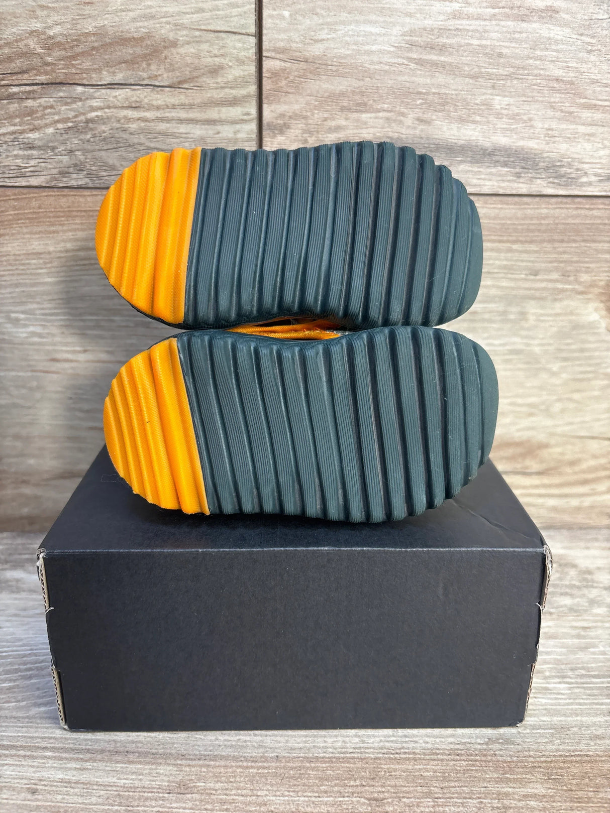 Pair of kids shoes with ribbed black and orange soles on a black box, wood background