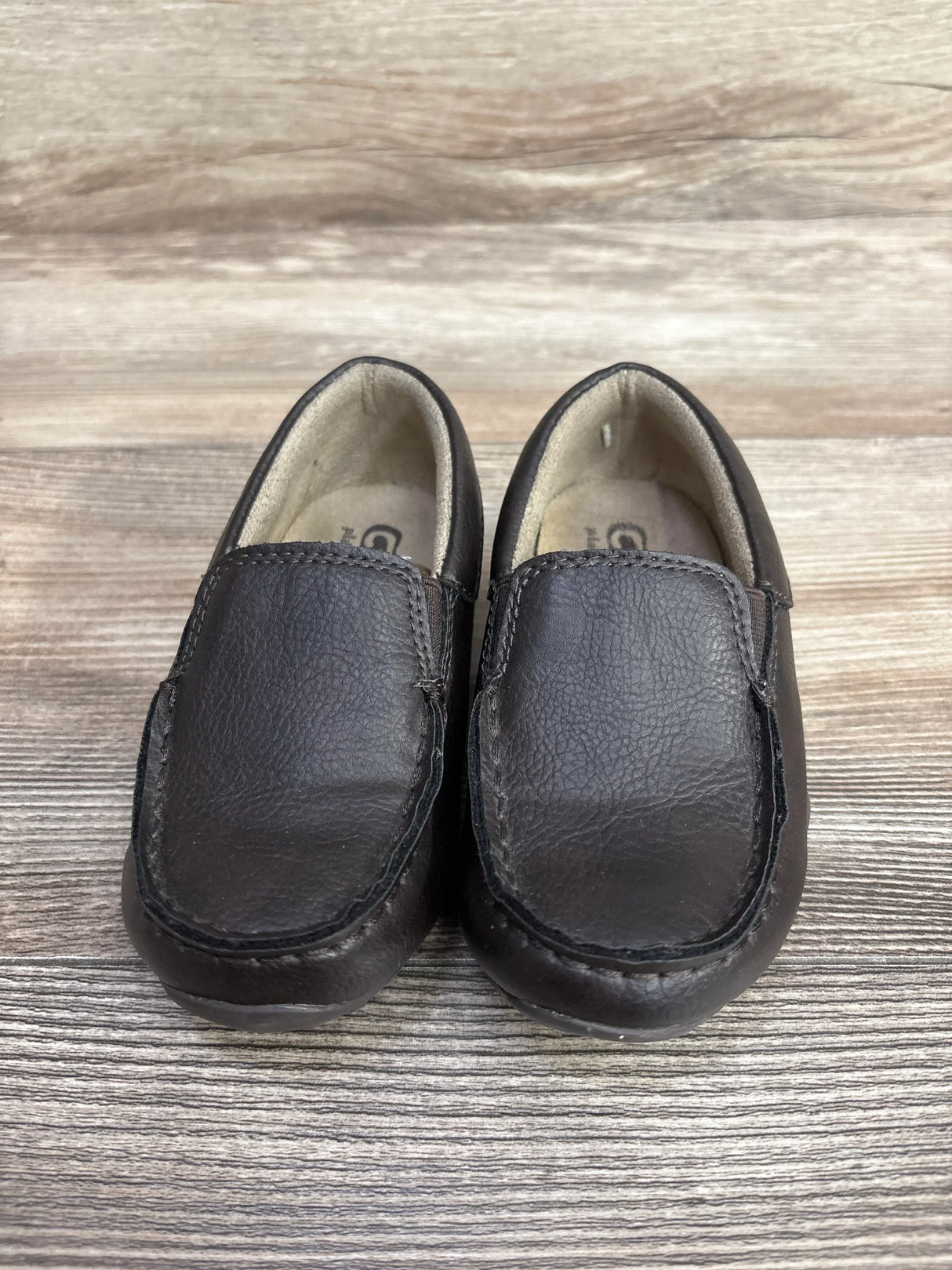 Front-top view of Children's Place brown slip-on dress shoes (size 8C) showing leather texture and light wear on wood background