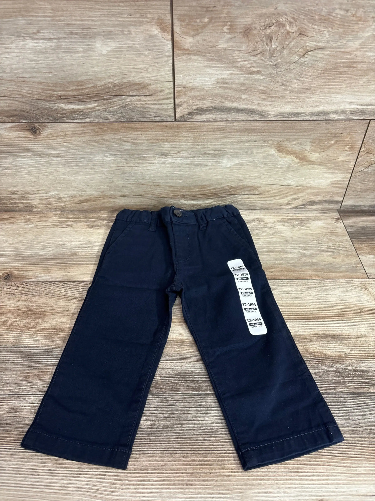 Front flat lay of navy Children’s Place chinos showing elastic waist with button, straight legs, size 12-18M sticker on wood