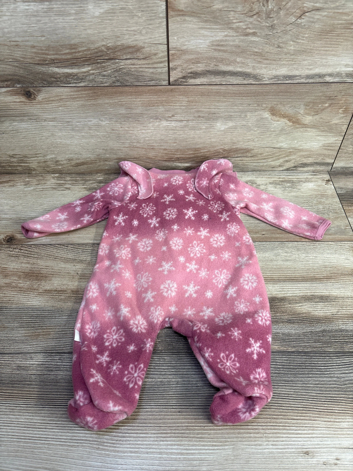 Pink fleece baby onesie with white snowflake pattern and long sleeves on wood floor