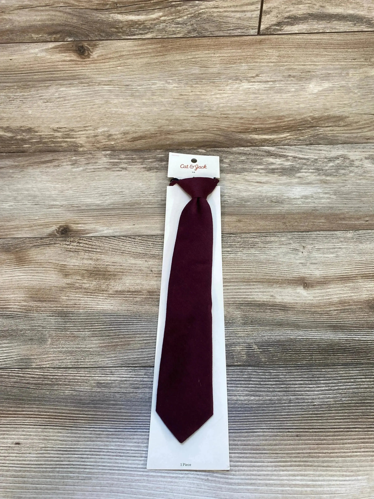 Top-down view of Cat and Jack wine zip-adjustable pre-tied necktie showing knot and narrow tip on light wood background
