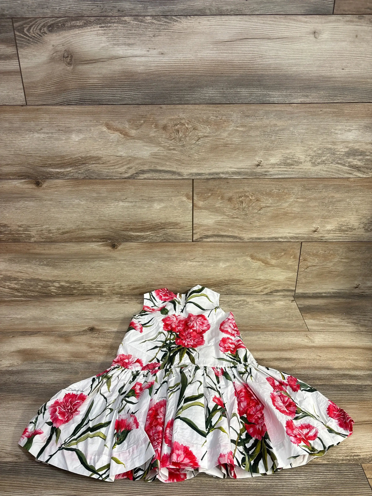 Flat lay of girls Dolce & Gabbana drop-waist poplin dress with pink carnation print and gathered skirt on wood floor