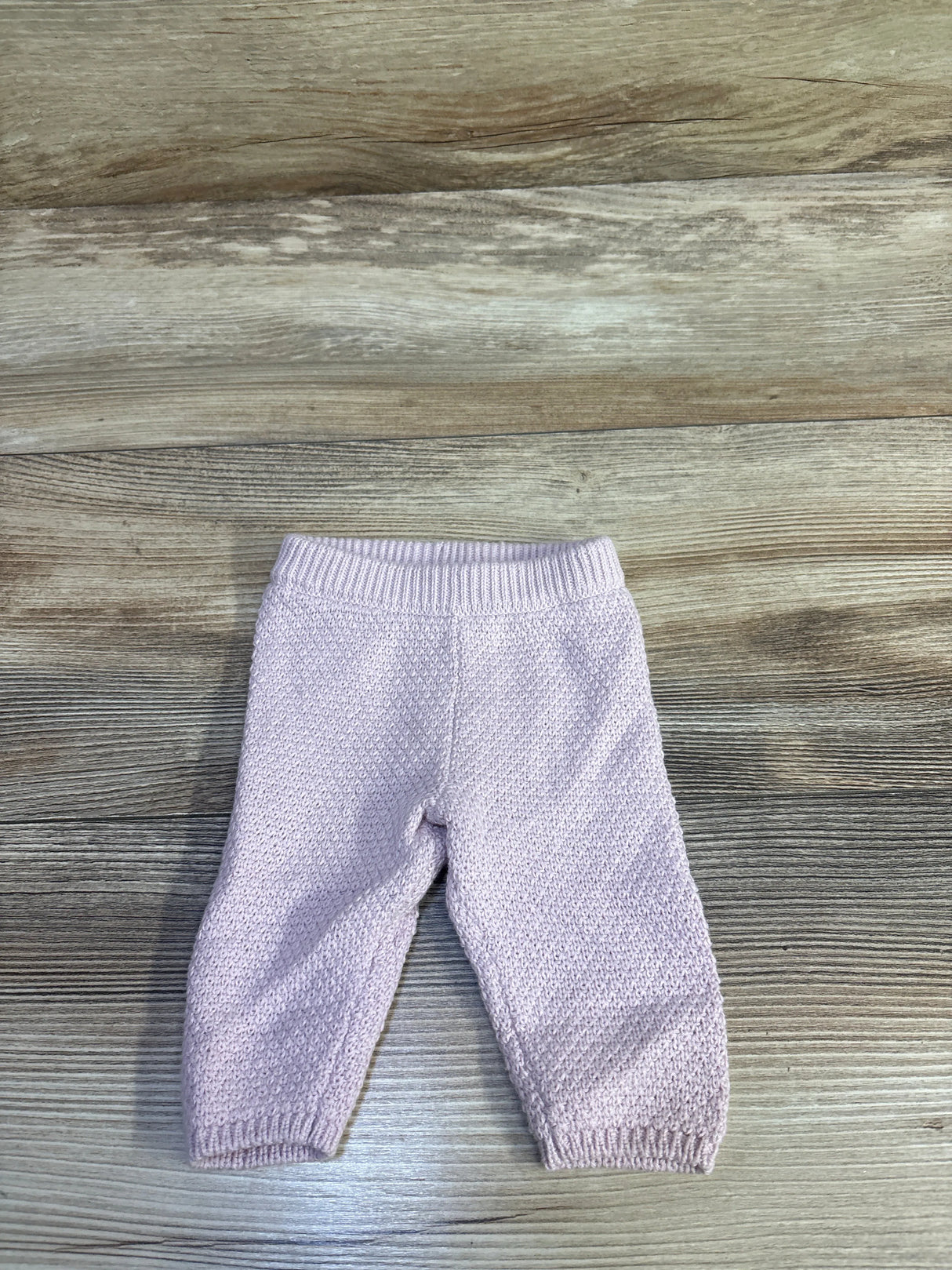 Top down view of newborn pink Little Planet knit pants showing textured stitch and ribbed waistband on wood floor