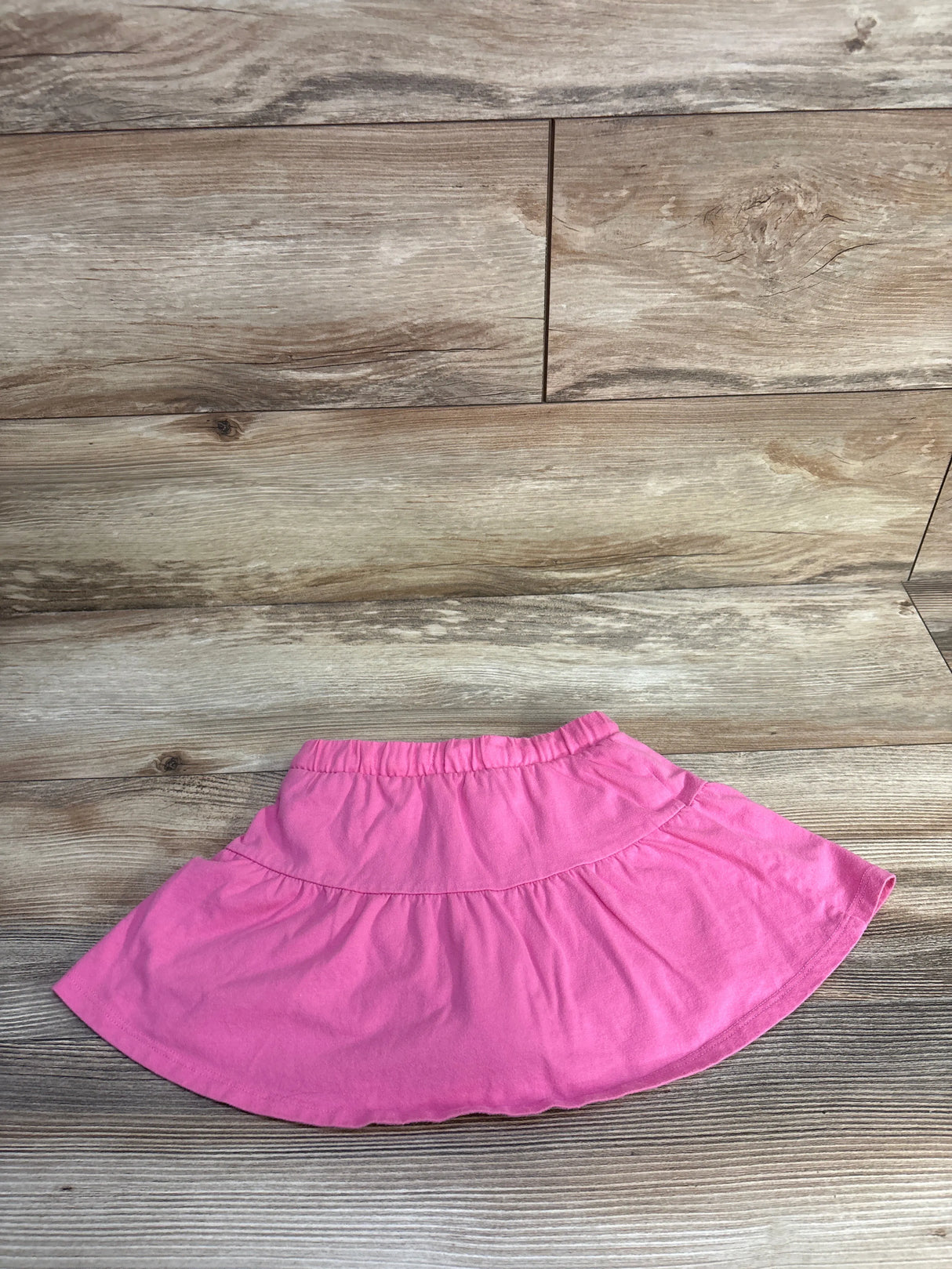 Flat-lay of girls' Jumping Beans pink skort showing elastic waistband and tiered skirt on wood background