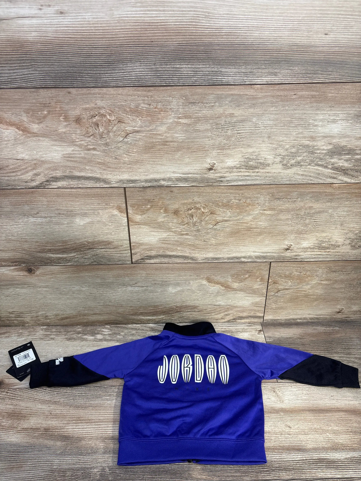 Back view of purple Jordan full-zip track jacket showcasing white Jordan lettering and black sleeves on a wood floor
