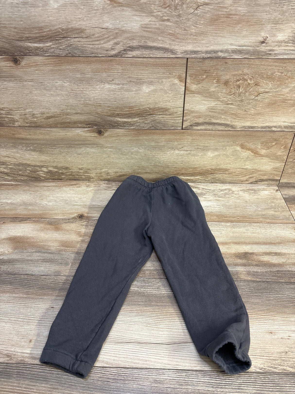 Flat lay of grey toddler jogger pants showcasing elastic waistband and cuffed ankles on wood floor background