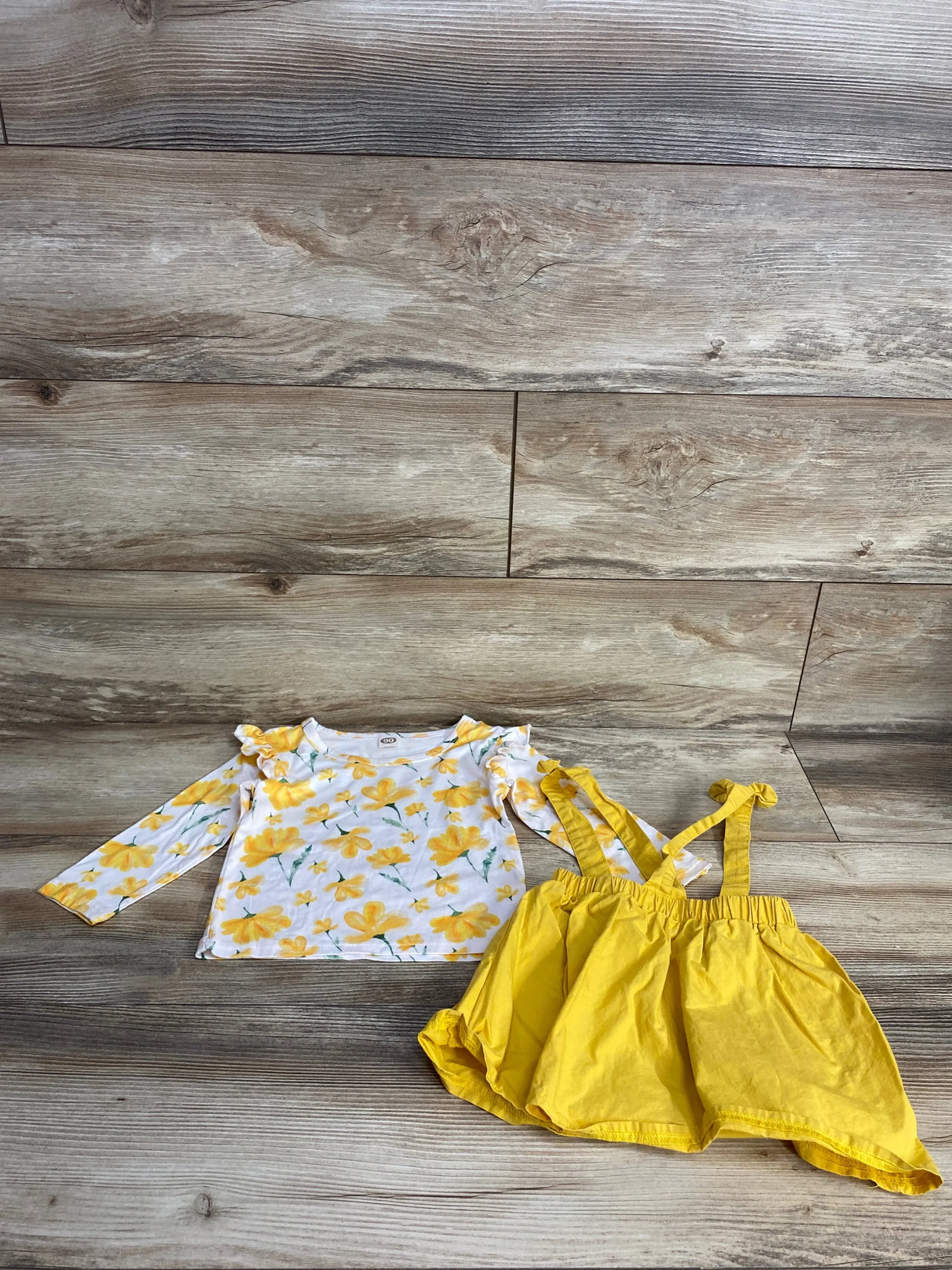Yellow floral long sleeve toddler shirt with matching yellow suspender skirt on wood floor