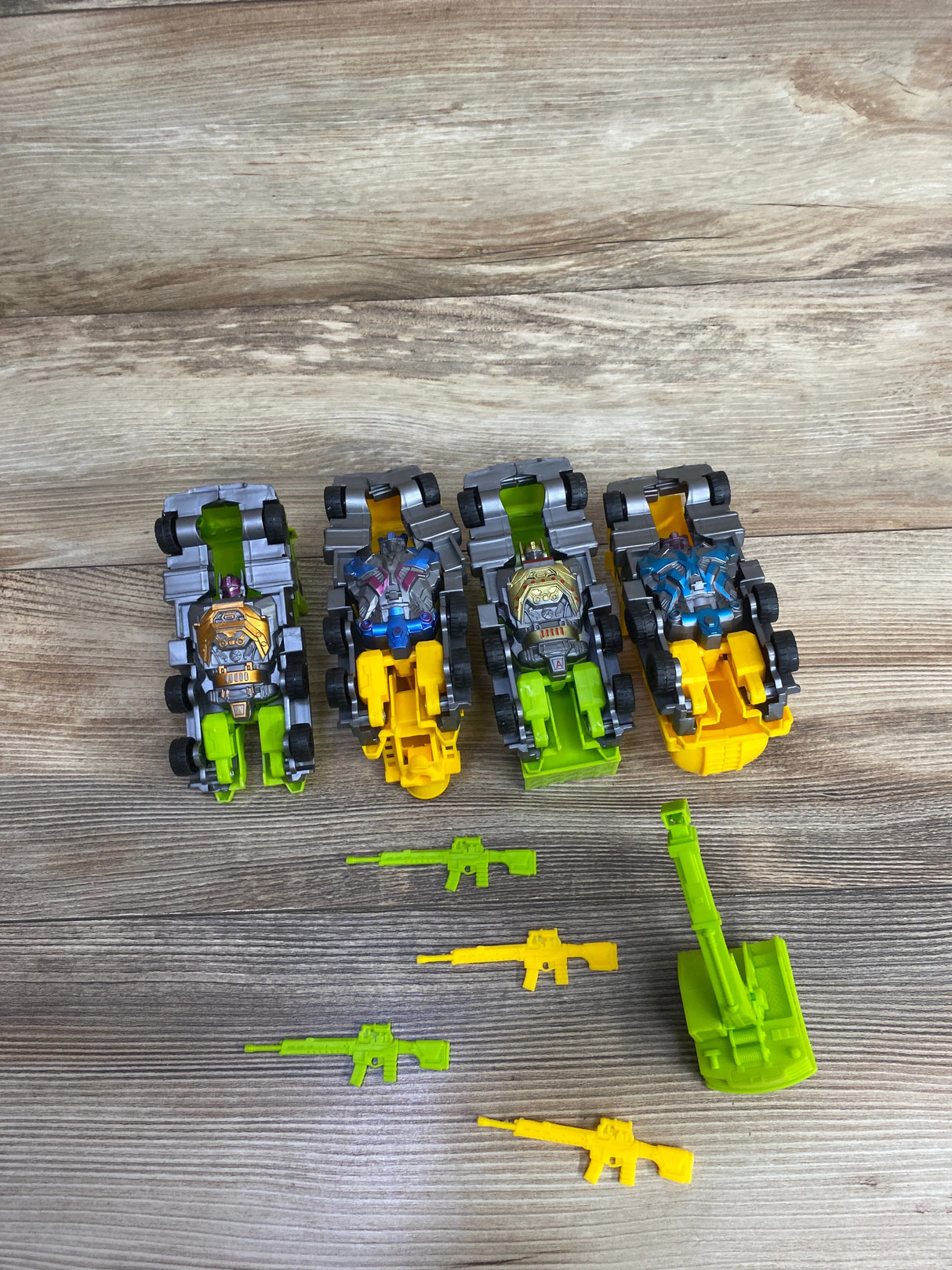 Four toy robot cars with yellow and green bases and small green and yellow toy guns on wood surface