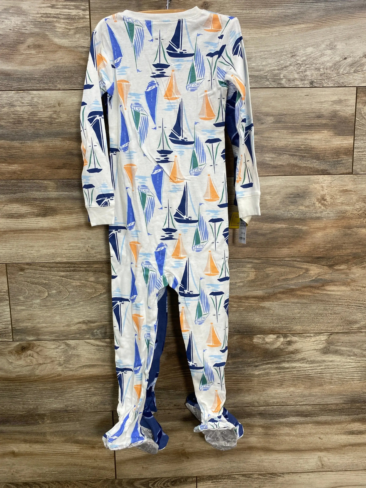 Front view of Just One You footed sleeper showcasing colorful sailboat print with wooden floor background