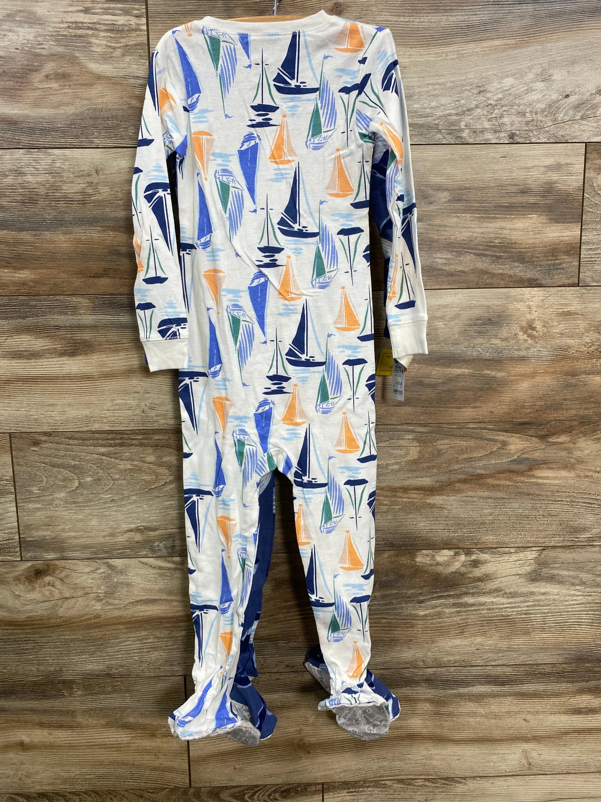 Children's white footed pajamas with colorful sailboat print on wooden floor