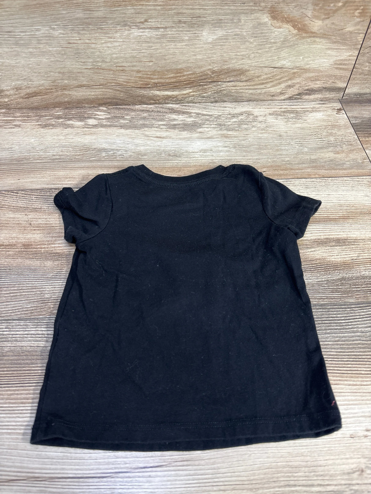 Black toddler short sleeve t-shirt laid flat on wood floor, kids clothing resale
