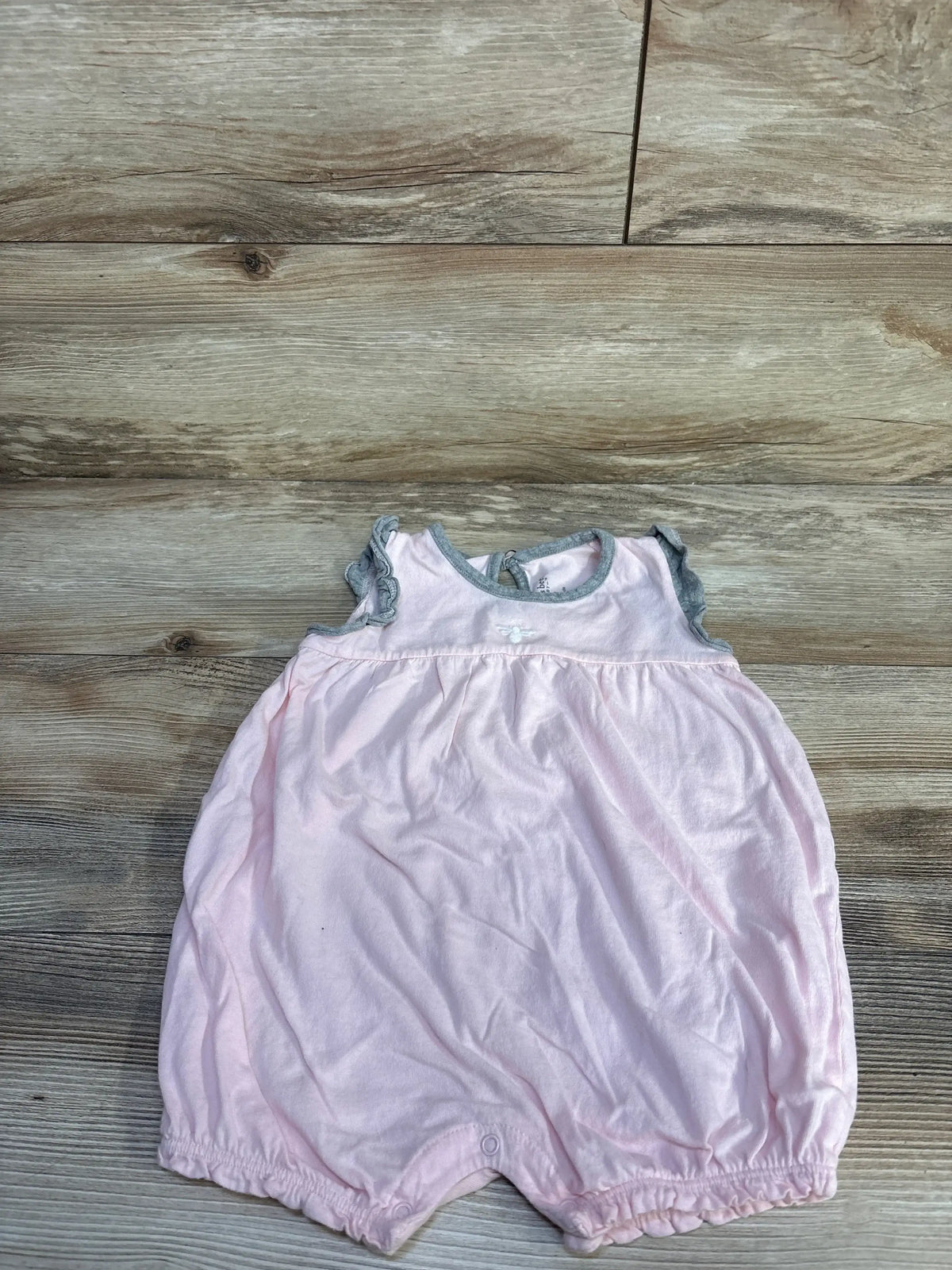 Flat lay of pink Burt’s Bees Baby shortie romper showcasing ruffled gray-trim sleeves and snap crotch on wood plank background