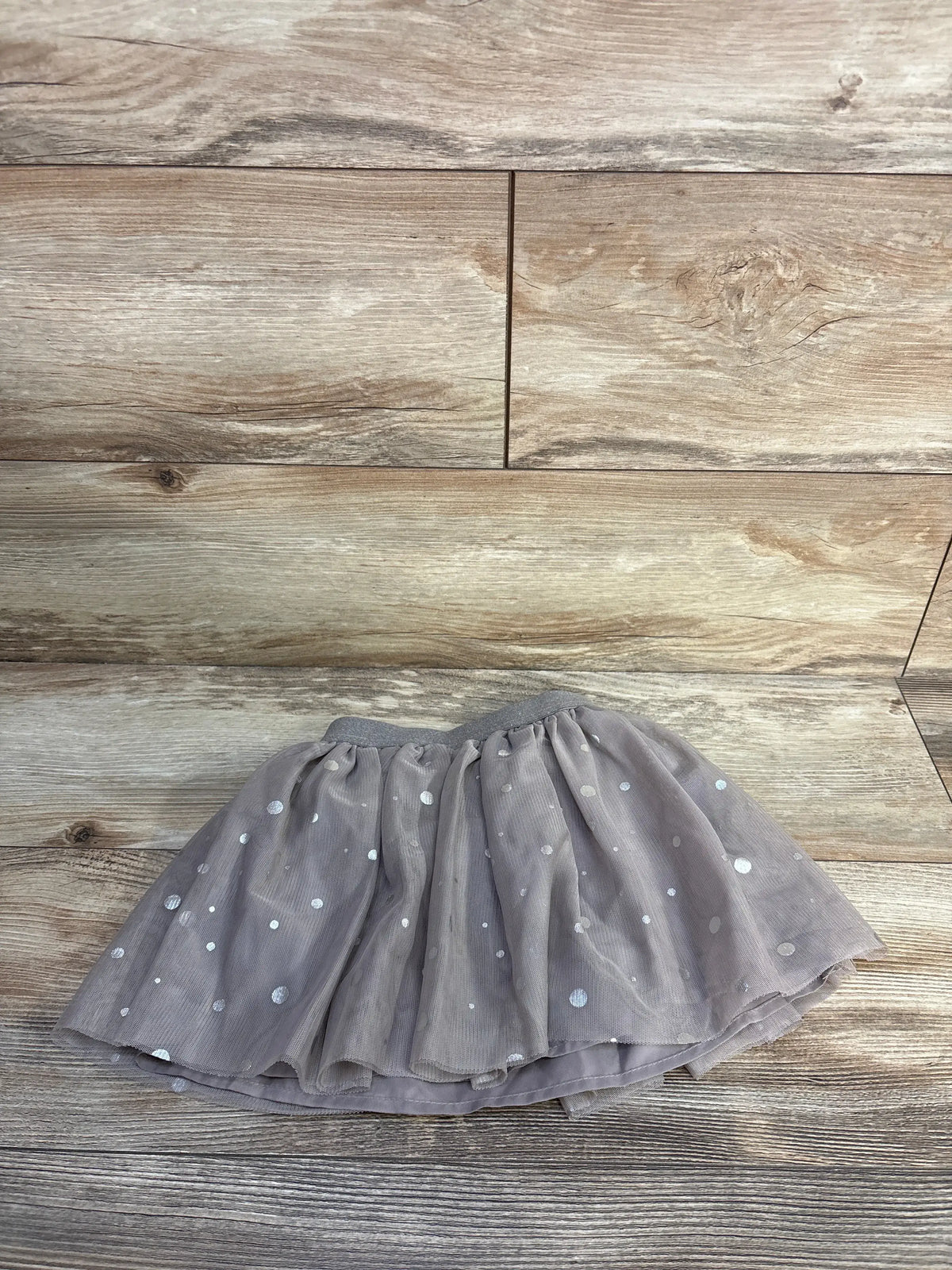 Front view of brown H&M polka dot tulle skirt showcasing elasticized waistband and ruffle trim on wood-grain background