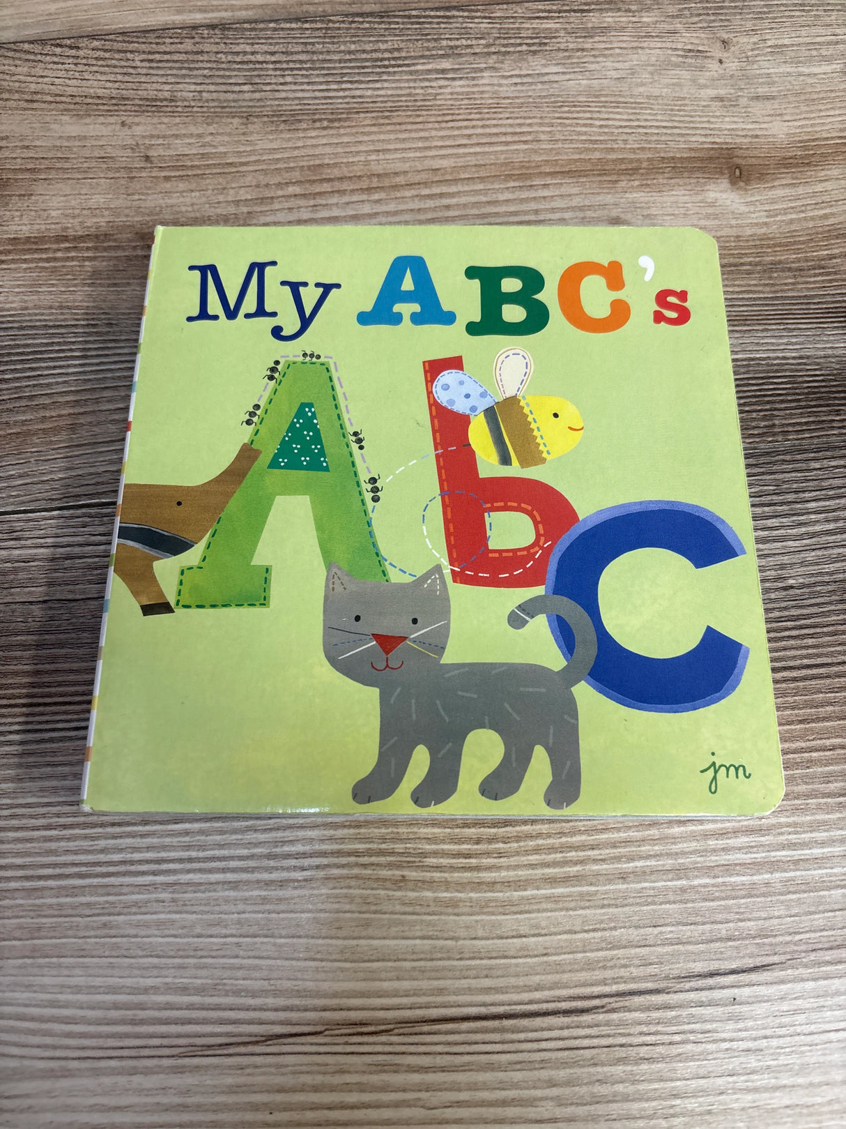 My ABC's board book cover with colorful letters, a cartoon cat, and a bee on wood table