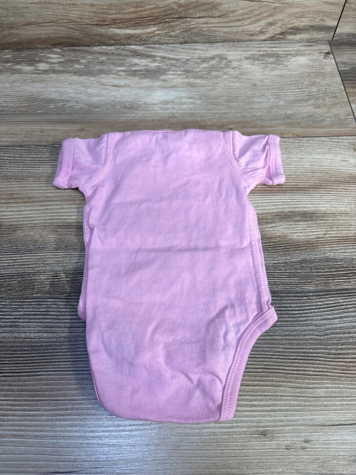 Top view of the pink Rabbit Skins newborn bodysuit showcasing short sleeves and rounded leg openings on a wood-grain background