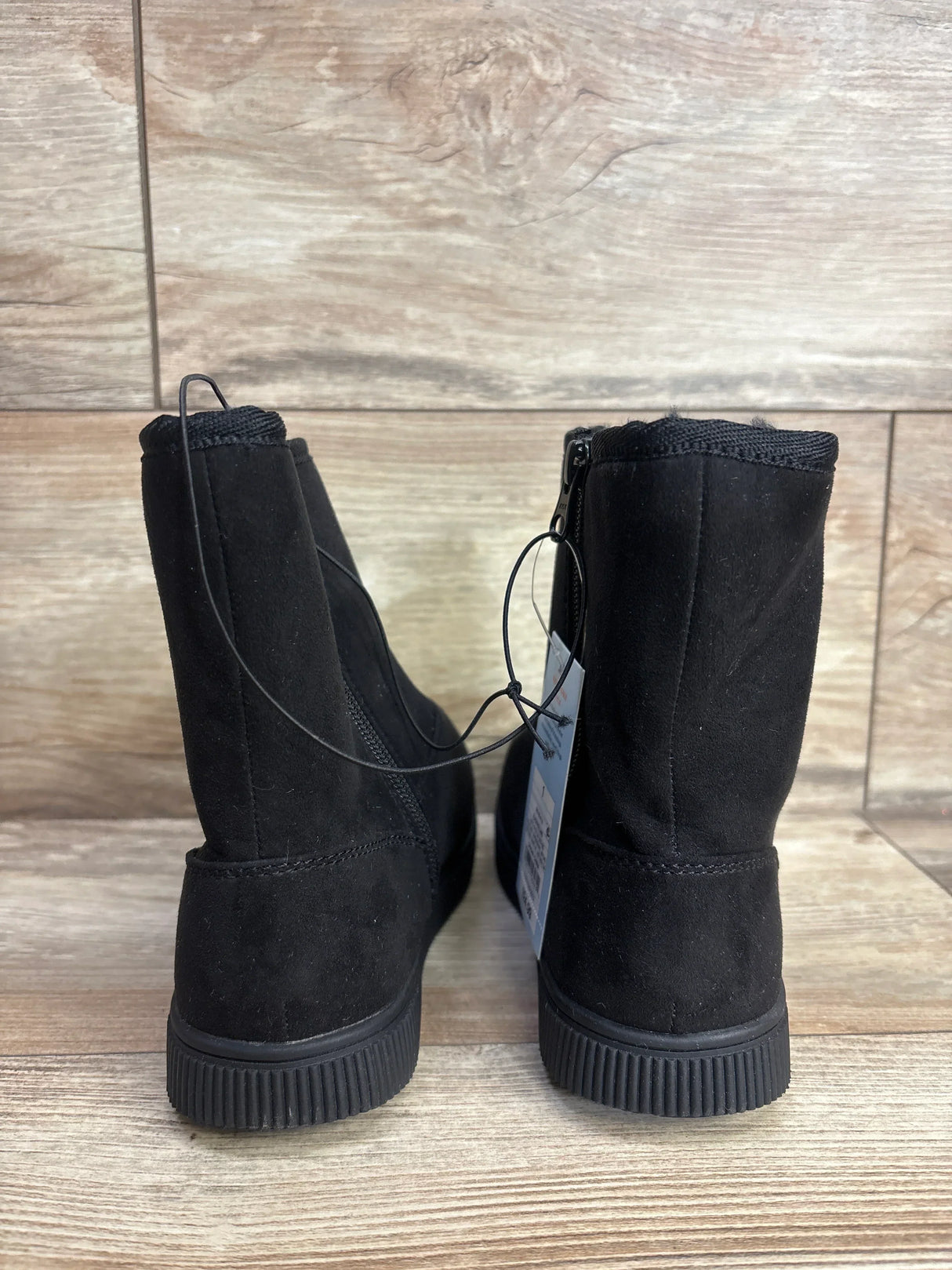 Black kids suede short boots with flat soles on wood floor, rear view