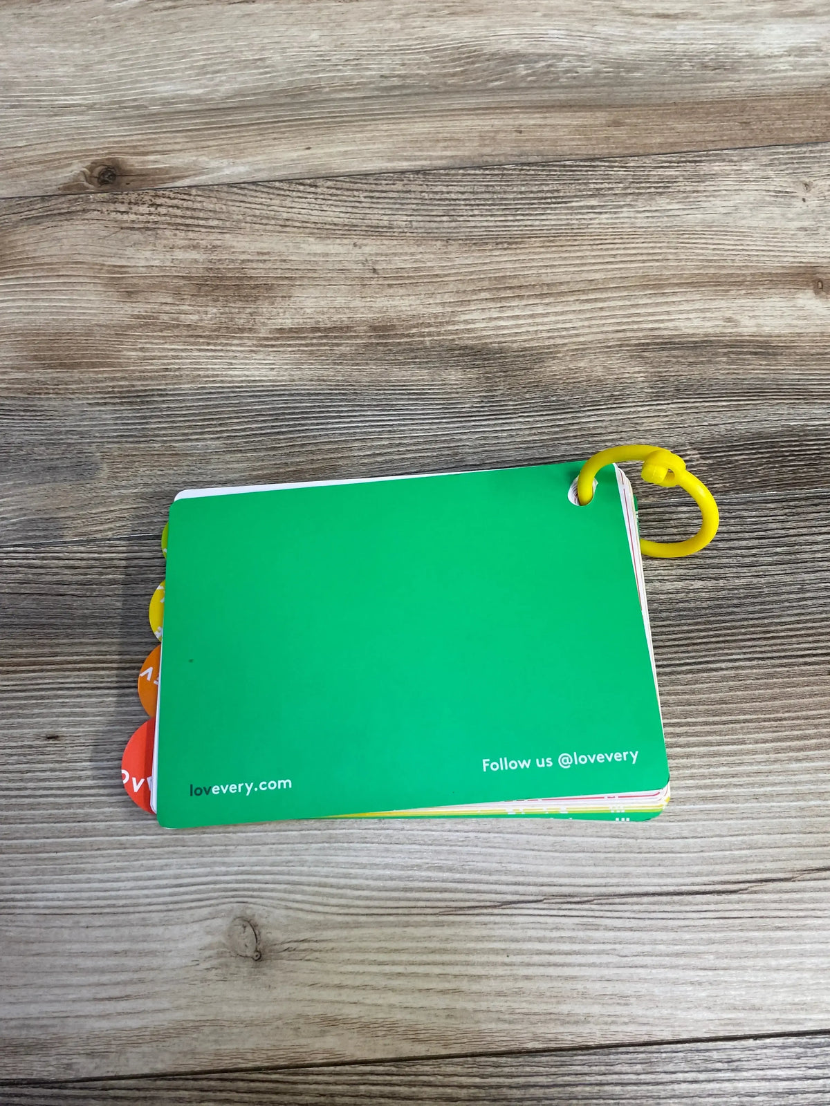 Top view of Lovevery The Thinker play guide flashcards showing green cover and yellow plastic ring on wooden surface