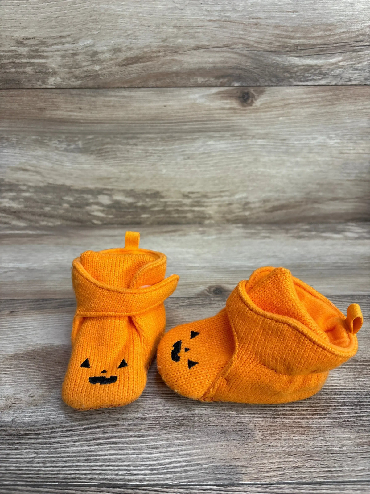 Orange baby booties with black jack-o'-lantern faces, Halloween themed on wood background
