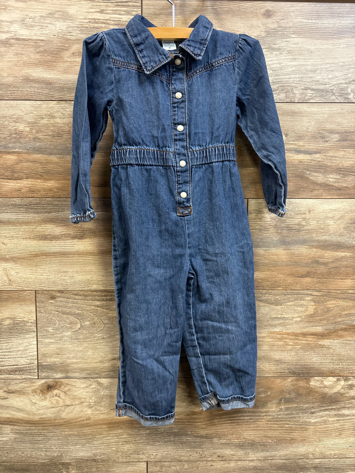Front view of chambray polo coverall showing snap-front buttons, elasticized waist, and long sleeves on wood background
