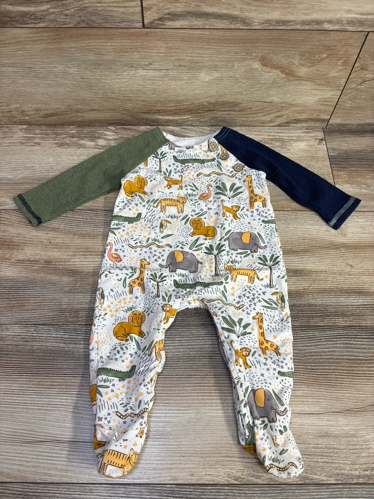 Baby sleeper with safari animal print, green and navy sleeves on wood floor