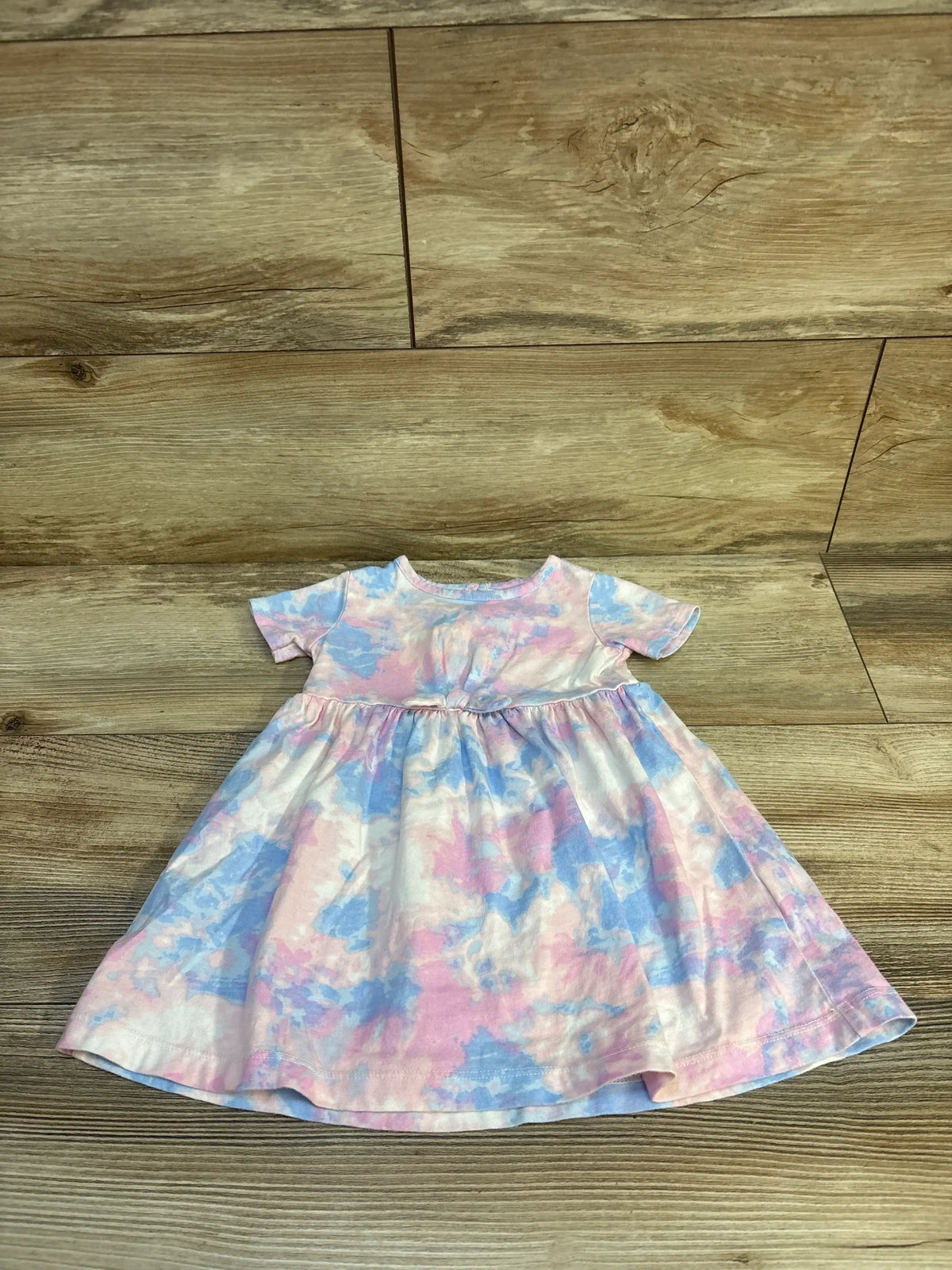 Flat lay of Carters pink and blue tie dye short sleeve fit and flare baby dress on wood plank floor