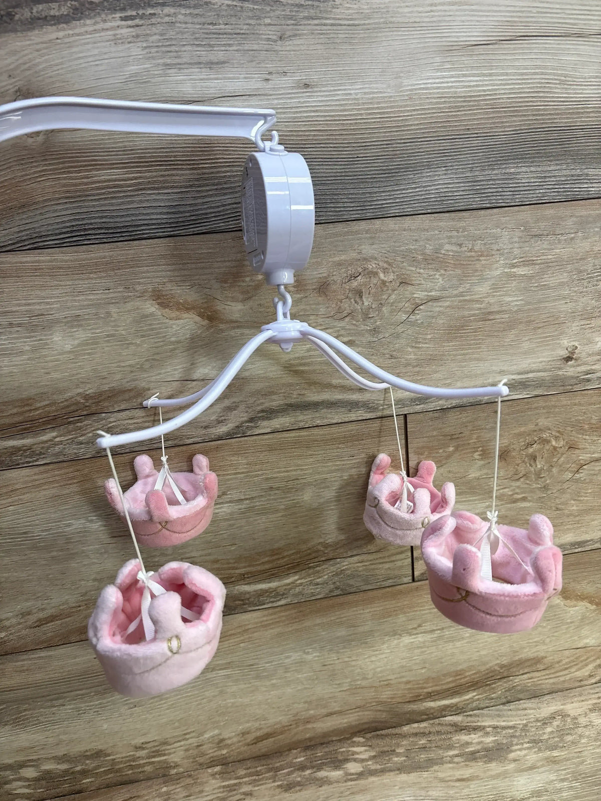 White baby mobile with four soft pink plush crown toys hanging against a wooden background