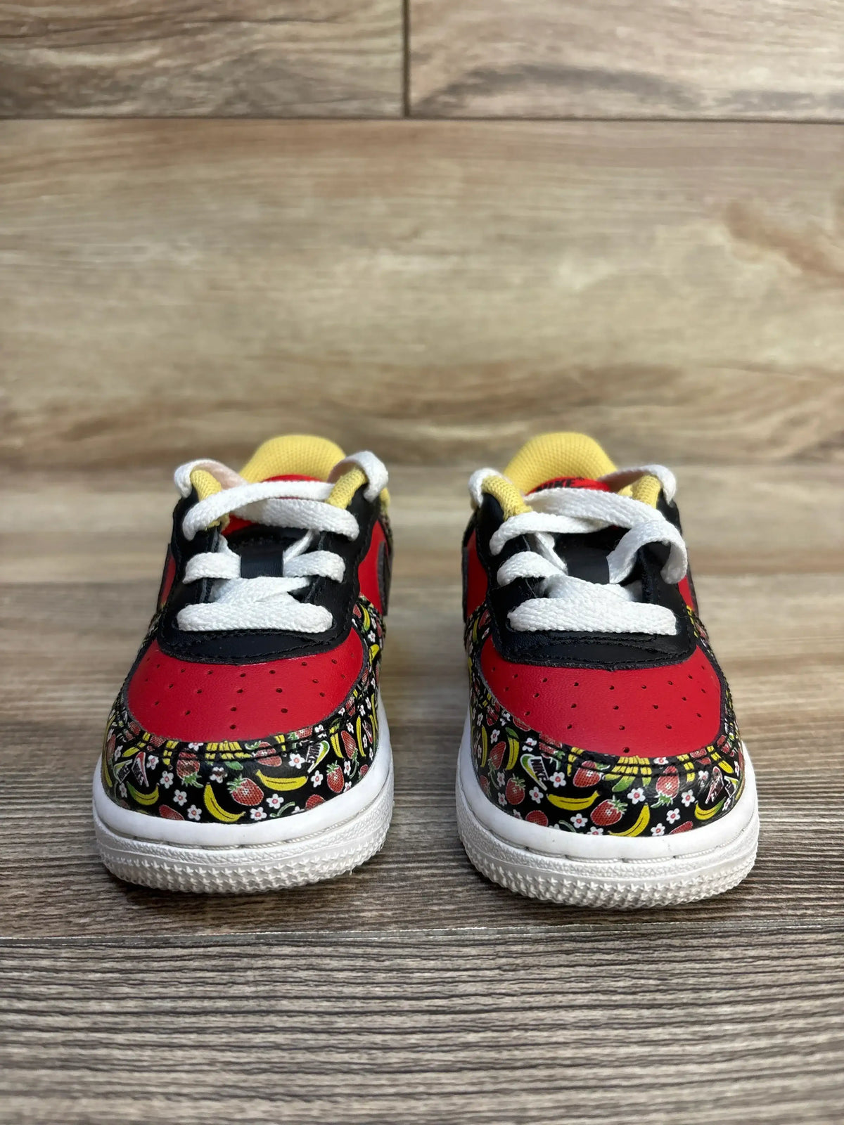 Kids' red and black sneakers with fruit print, white laces, yellow accents on wood floor
